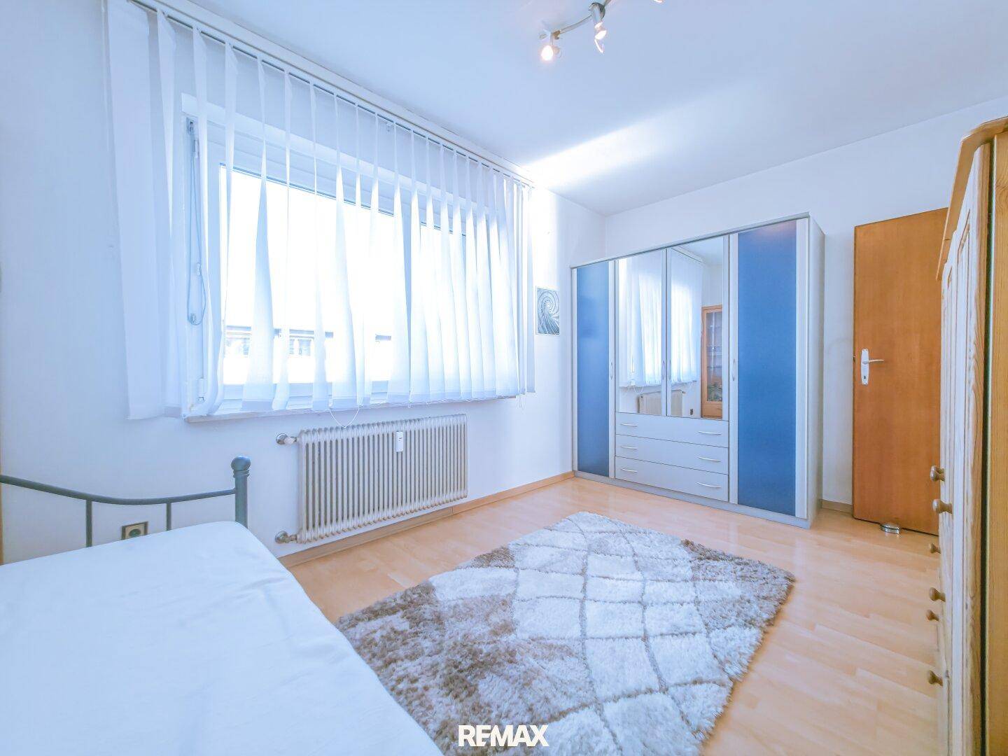 Helles Schlafzimmer mit großem Fenster, Parkettboden und Spiegelschrank.