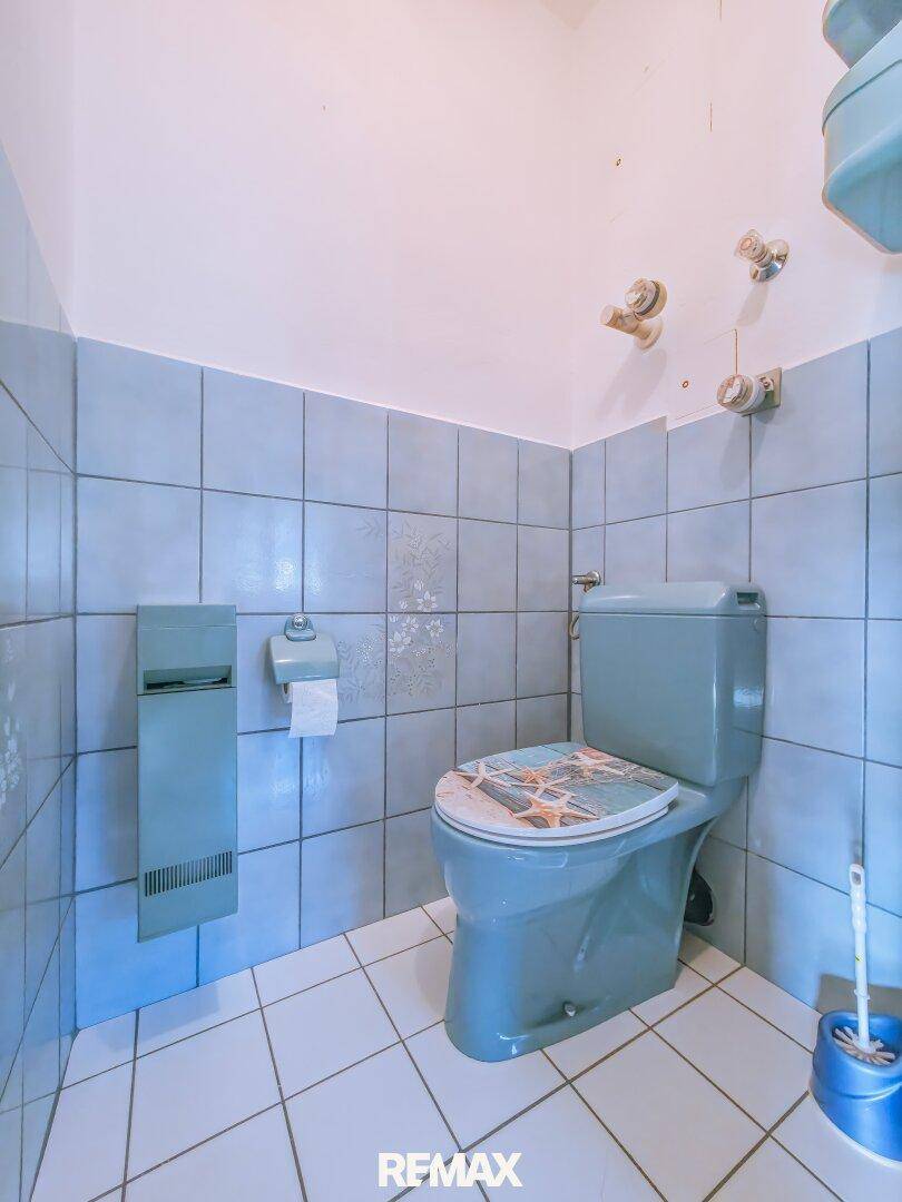 Separate Toilette mit blauen Fliesen und weißem Fliesenboden.