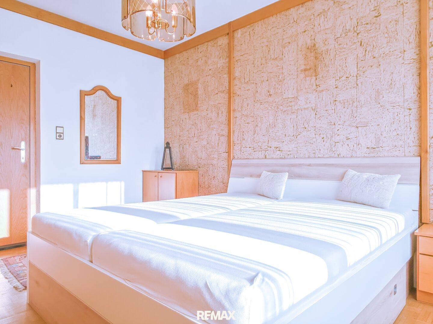 Helles Schlafzimmer mit Doppelbett, Holzboden und dekorativer Wandverkleidung.