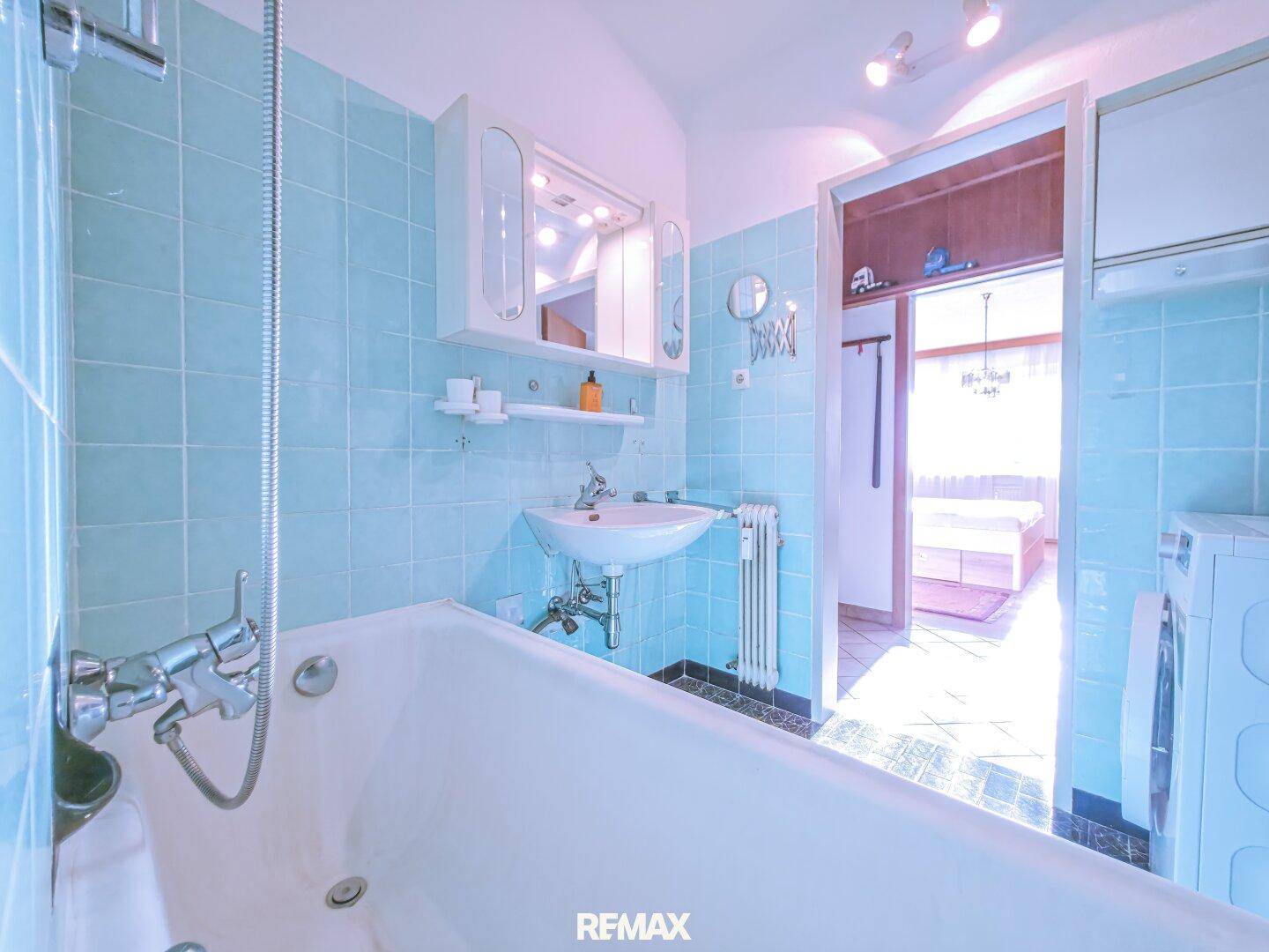 Badezimmer mit Badewanne, Waschbecken und Zugang zu einem weiteren Raum.