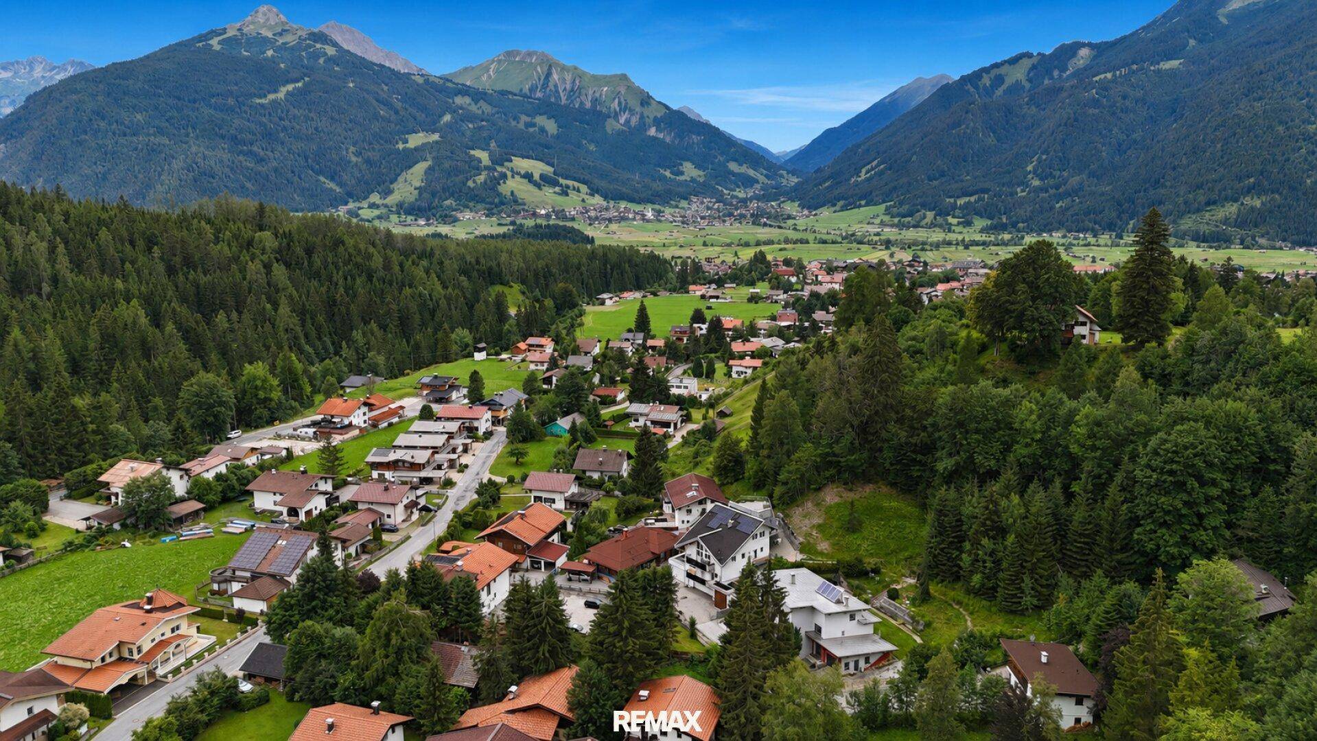 Weitläufige Luftaufnahme eines malerischen Dorfes in einem Tal, umgeben von Bergen und Wäldern.