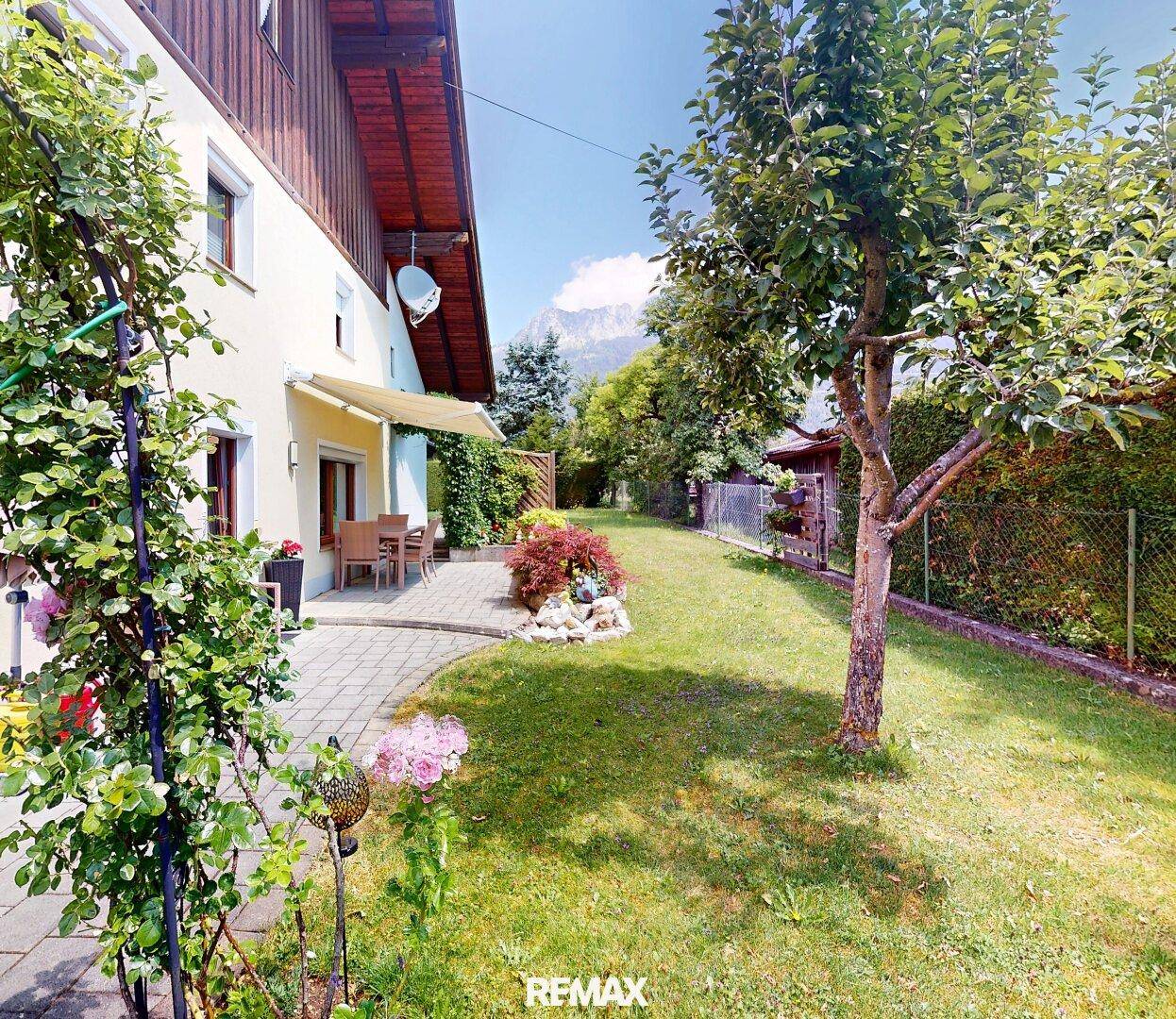 Sonniger Garten mit altem Obstbaum, Rasenfläche und Blick auf die Berge.