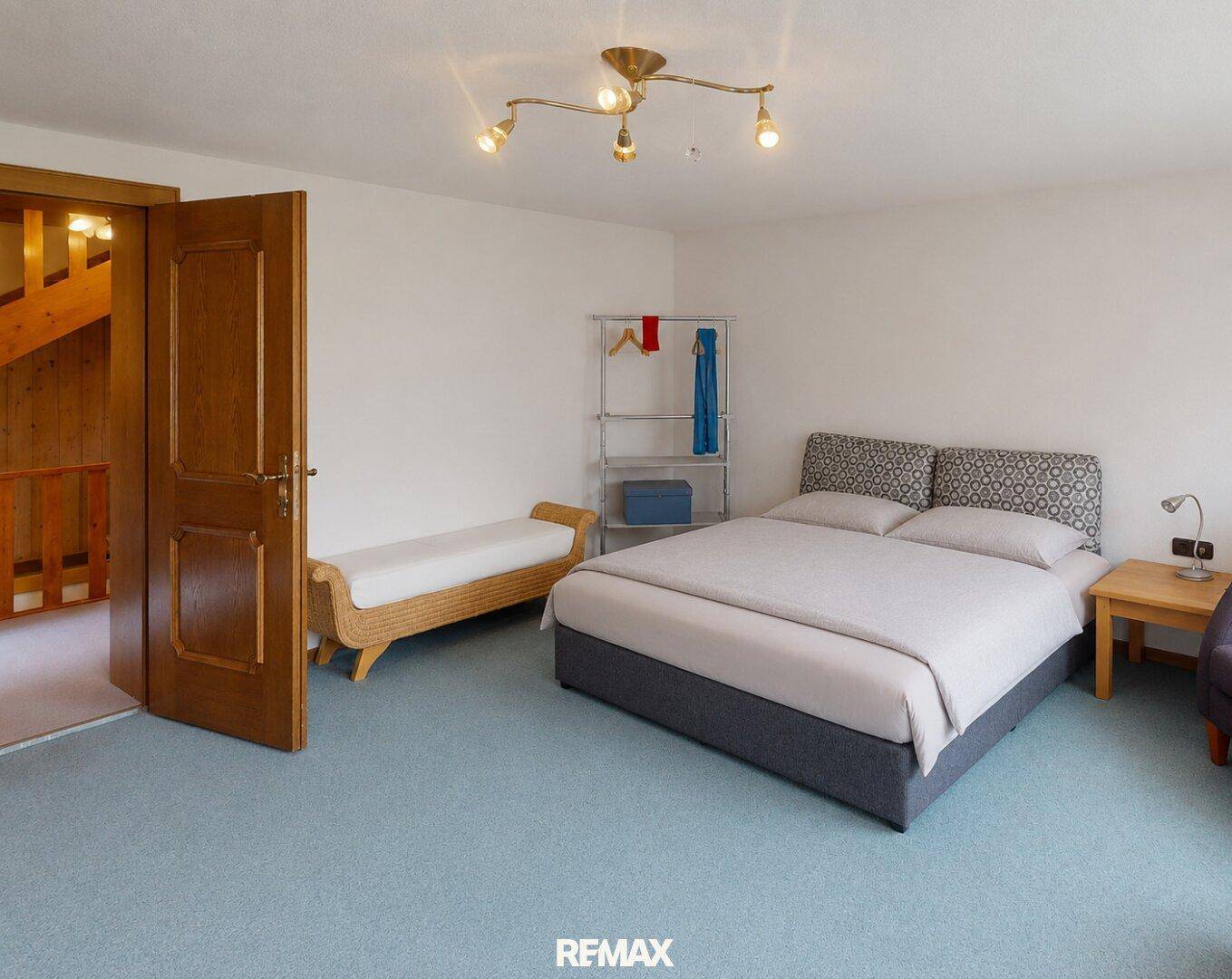 Helles Schlafzimmer mit Doppelbett, Teppichboden und Zugang zur Treppe.