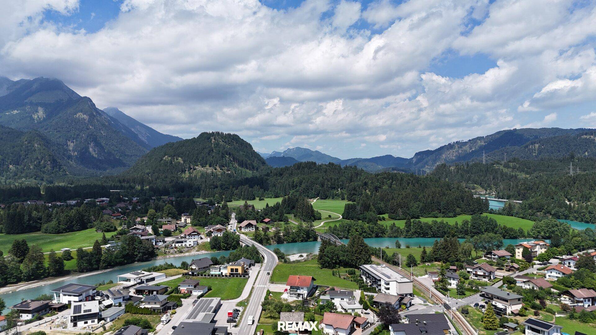 Weitläufige Luftaufnahme einer Siedlung mit Fluss, Bergen und grüner Umgebung.
