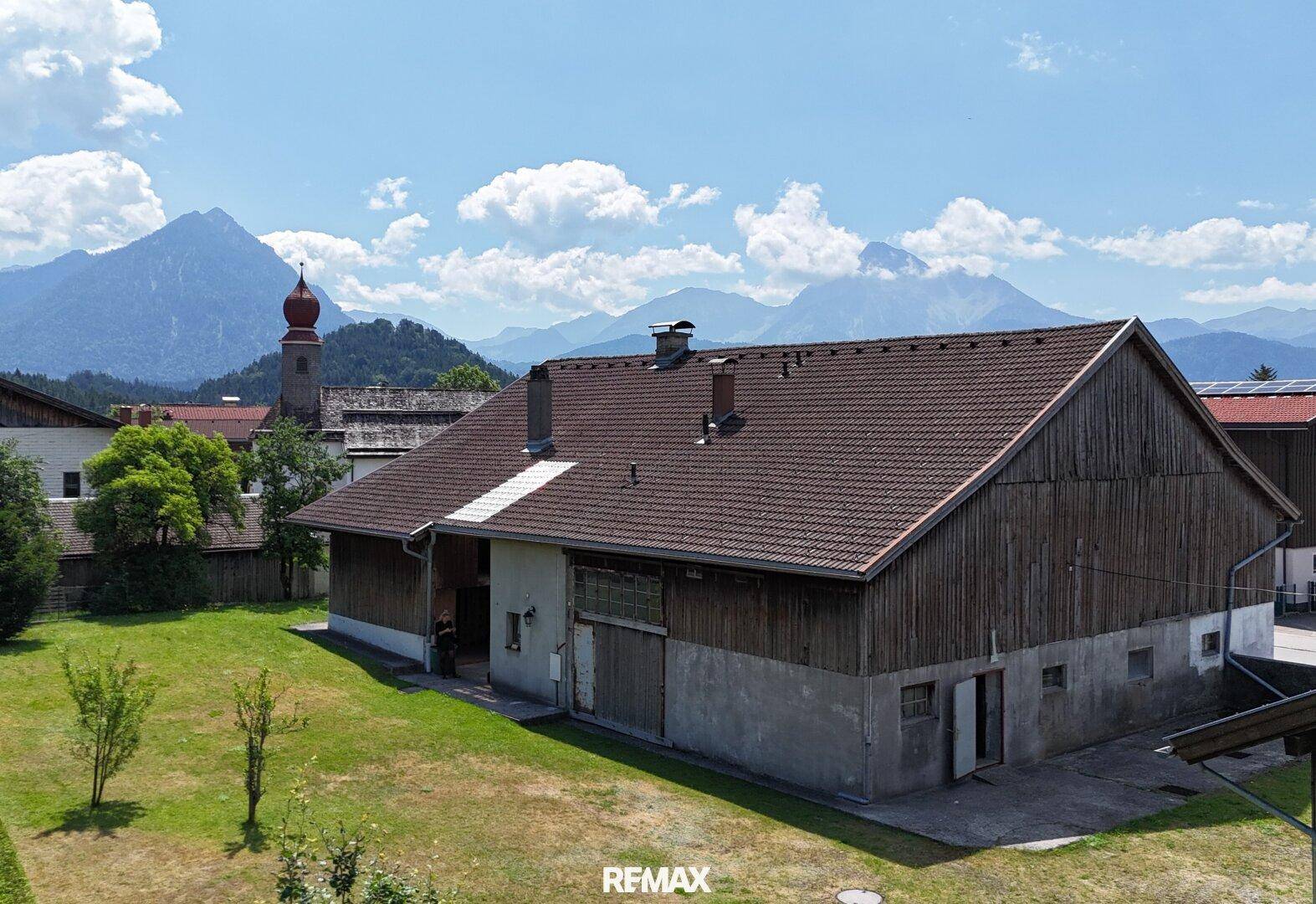 Großes Scheunengebäude mit Holzwänden und Blick auf die Kirche und Berge.