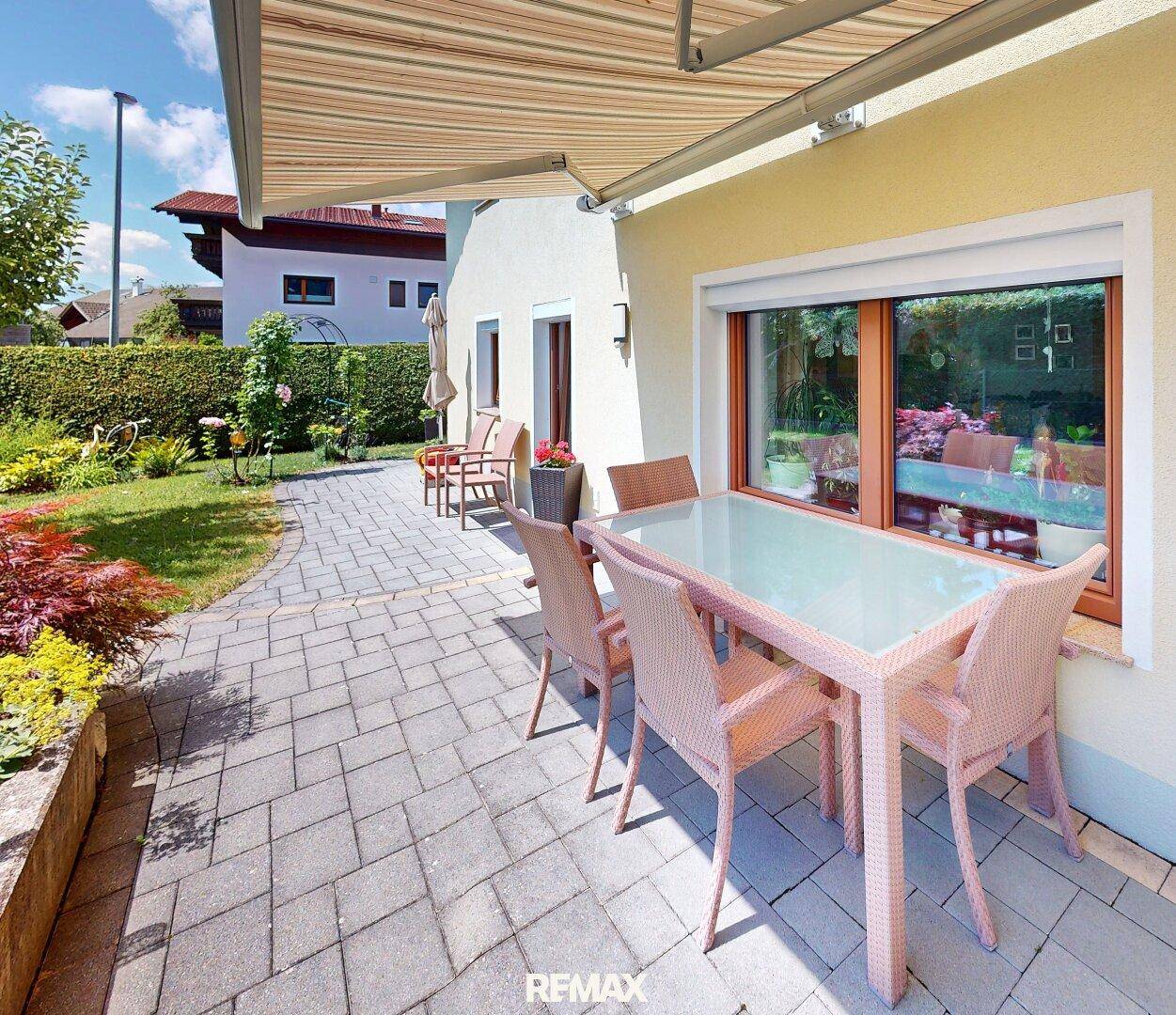Große gepflasterte Terrasse mit Markise, Gartenmöbeln und Blick in den Garten.