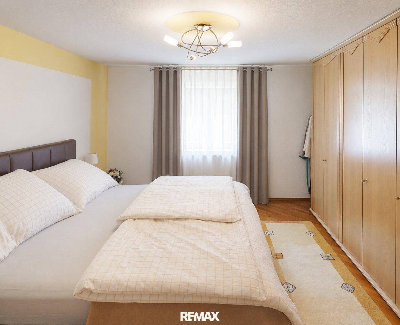 Gemütliches Schlafzimmer mit Doppelbett, Holzschrank und Fenster mit Vorhängen.