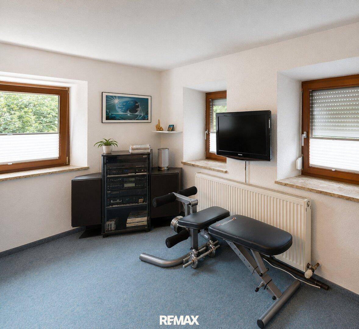 Kleiner Fitnessraum mit Trainingsbank, Fernseher und Teppichboden.