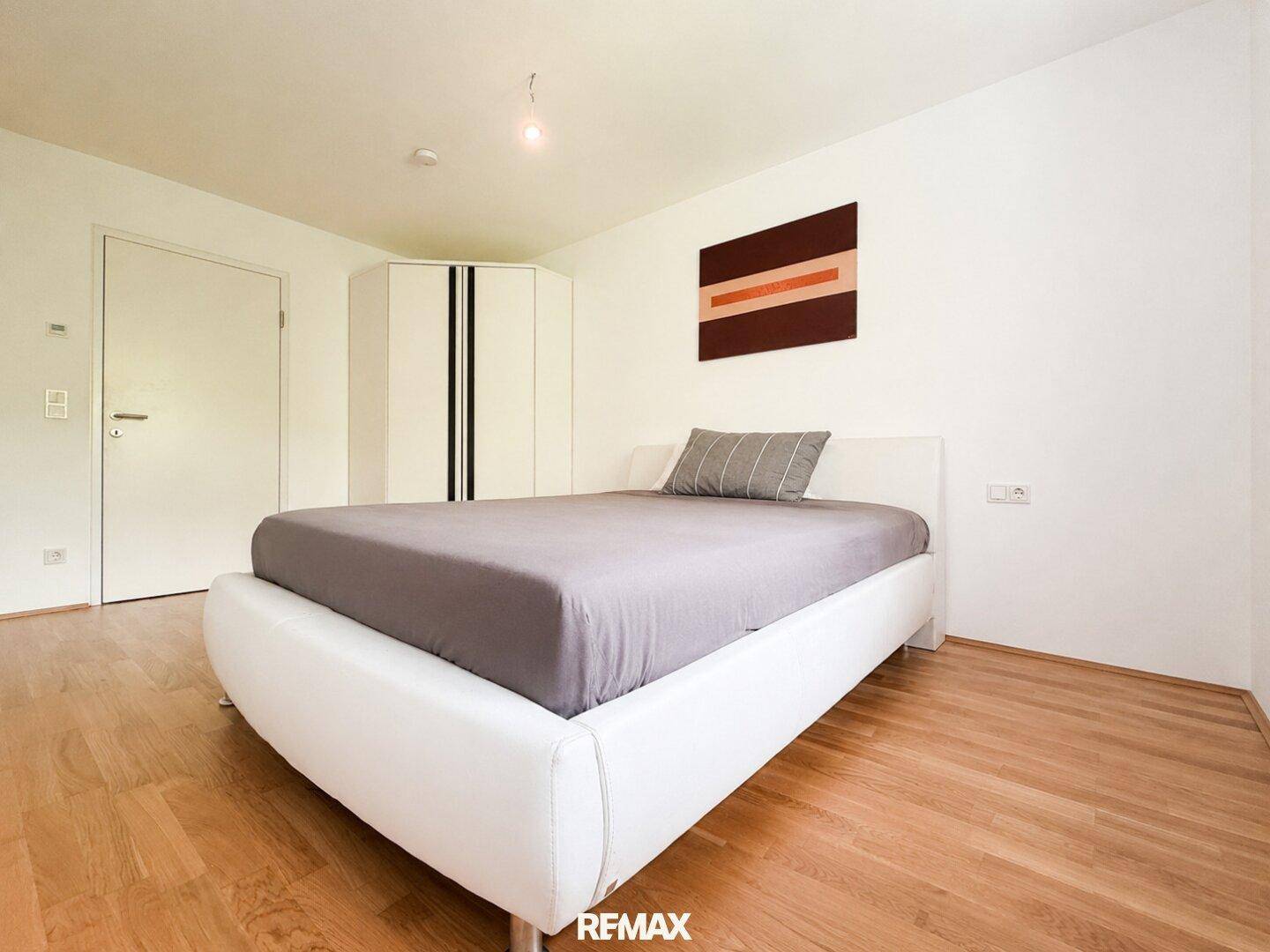 Geräumiges Schlafzimmer mit modernem Bett, Holzboden und einem praktischen Eckkleiderschrank.