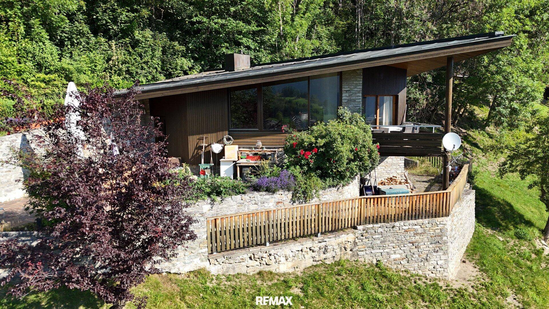 Das Haus mit seiner Steinfassade und Holzverkleidung ist von einem gepflegten Garten umgeben.