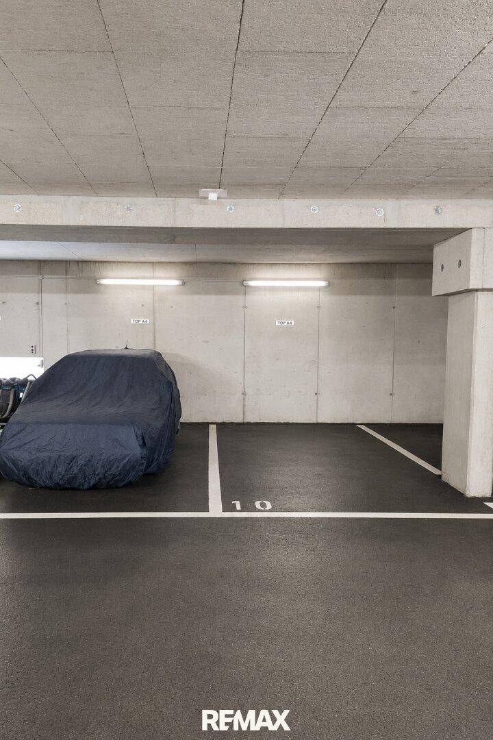 Geräumige Tiefgarage mit einem abgedeckten Fahrzeug und einem freien Stellplatz in sauberem Zustand.