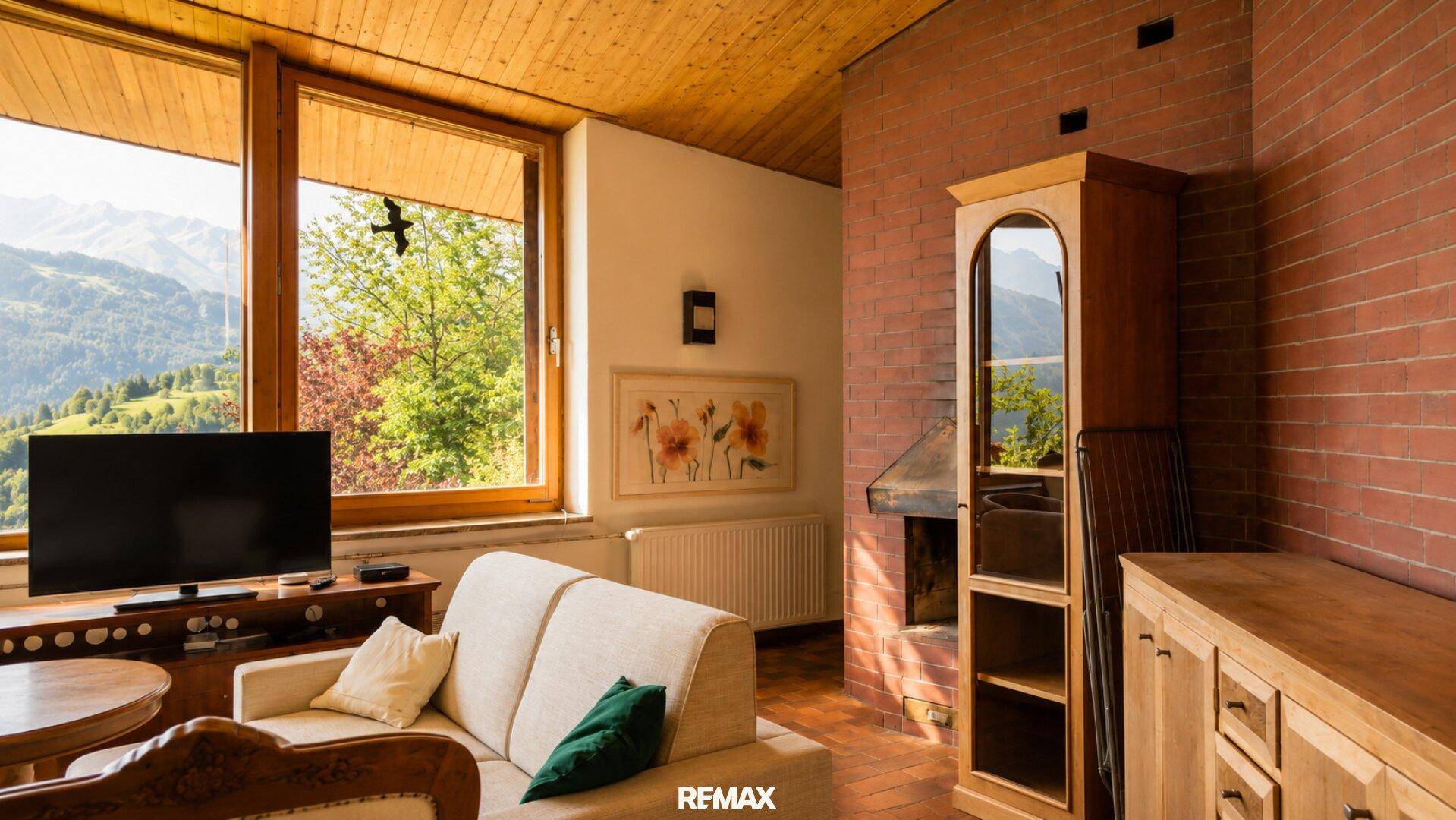 Gemütliches Wohnzimmer mit Sofa, Fernseher und großen Fenstern mit Bergblick.