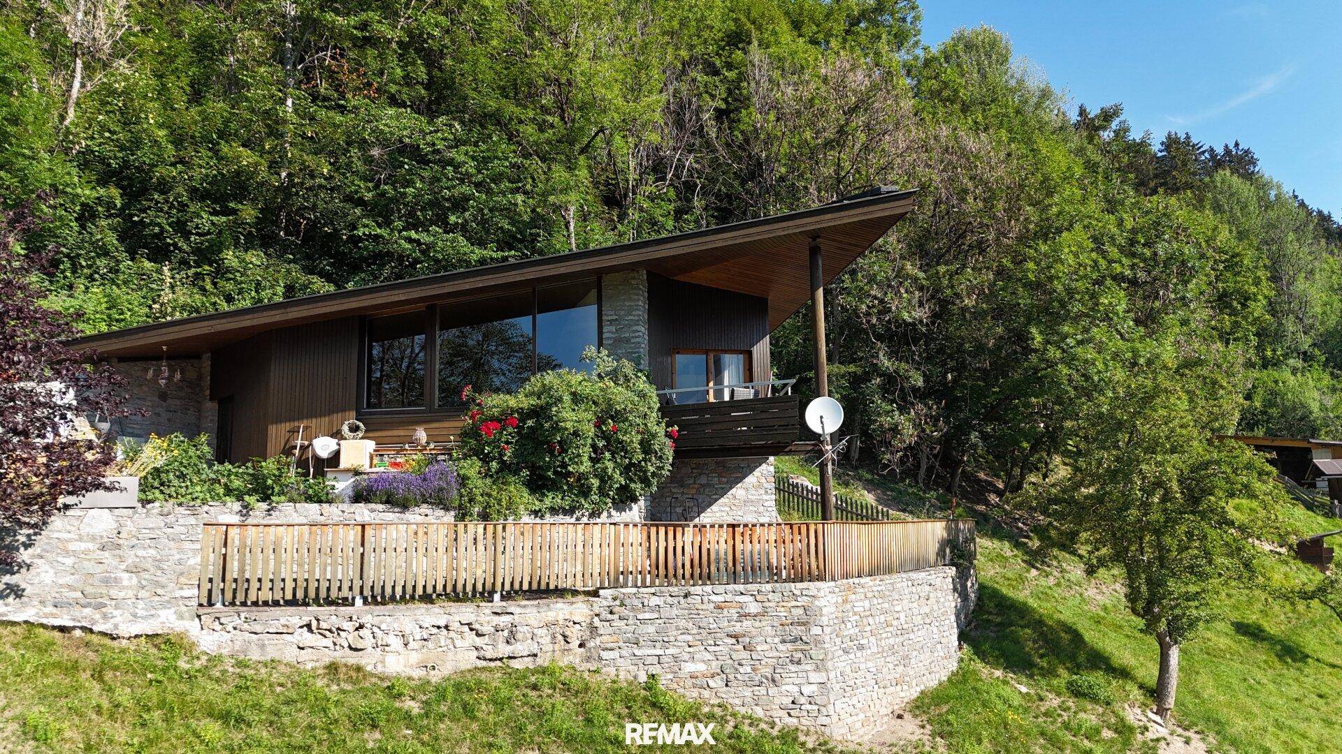 Das Haus fügt sich mit seiner Holz- und Steinfassade perfekt in die grüne Hanglandschaft ein.