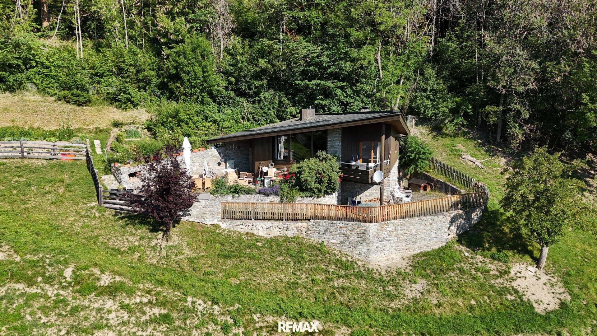 Das Haus mit seiner Steinfassade und dem terrassierten Gartenbereich in der grünen Umgebung.