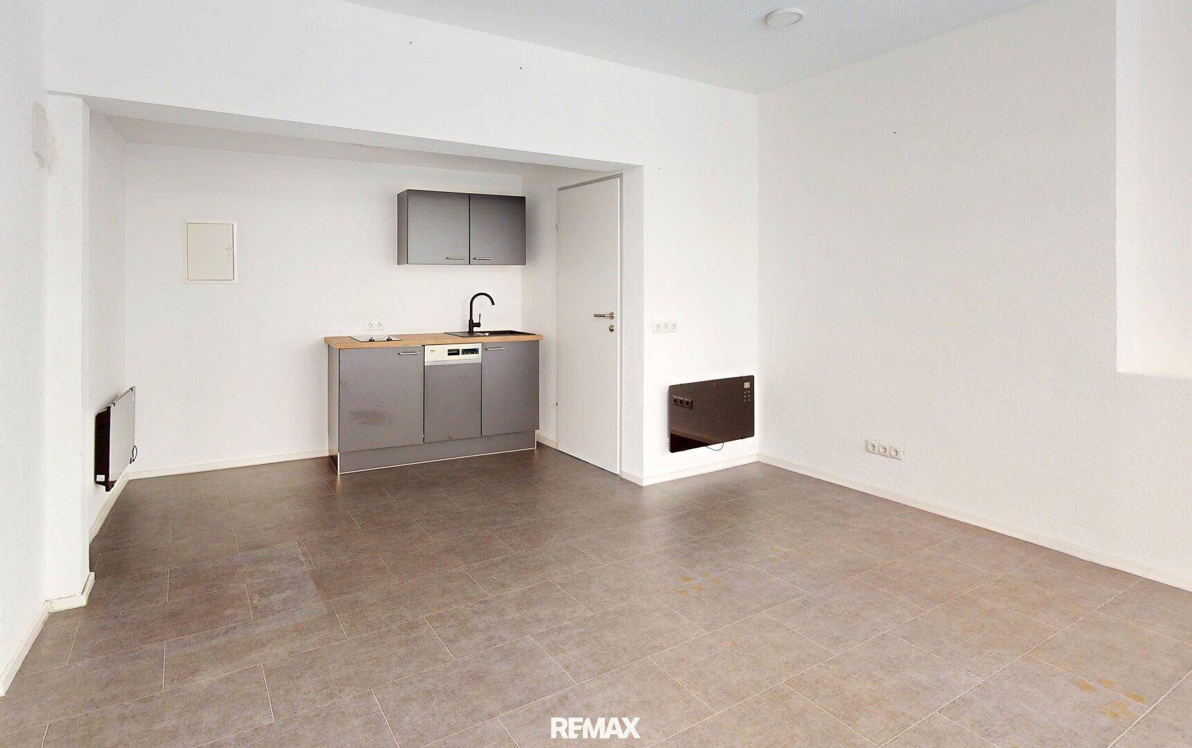 Heller Raum mit Küchenzeile, Fliesenboden und einer Tür, ideal für ein Studio-Apartment.