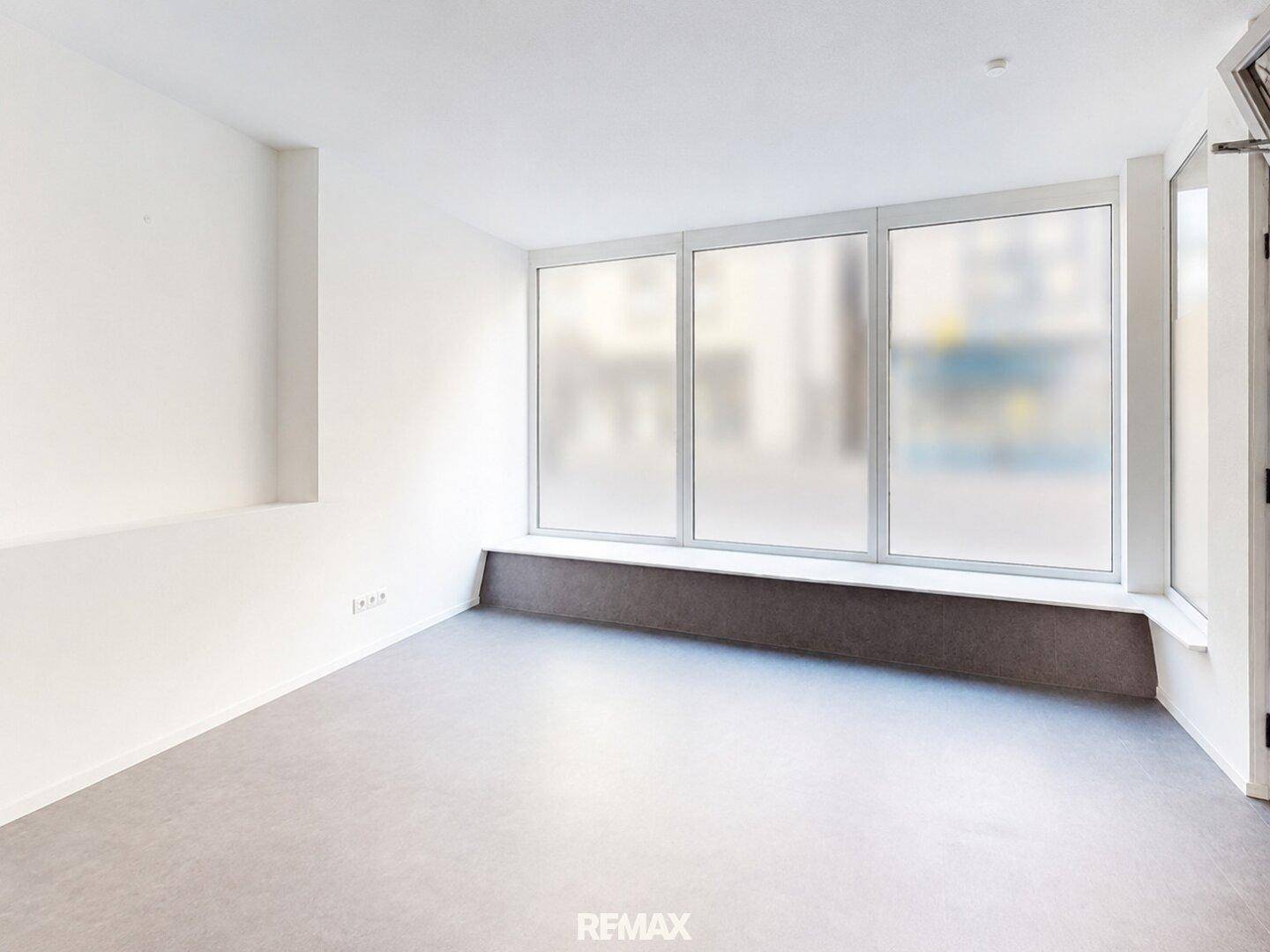 Leerer Raum mit großen, blickdichten Fenstern und hellem Boden, ideal für ein ruhiges Büro.