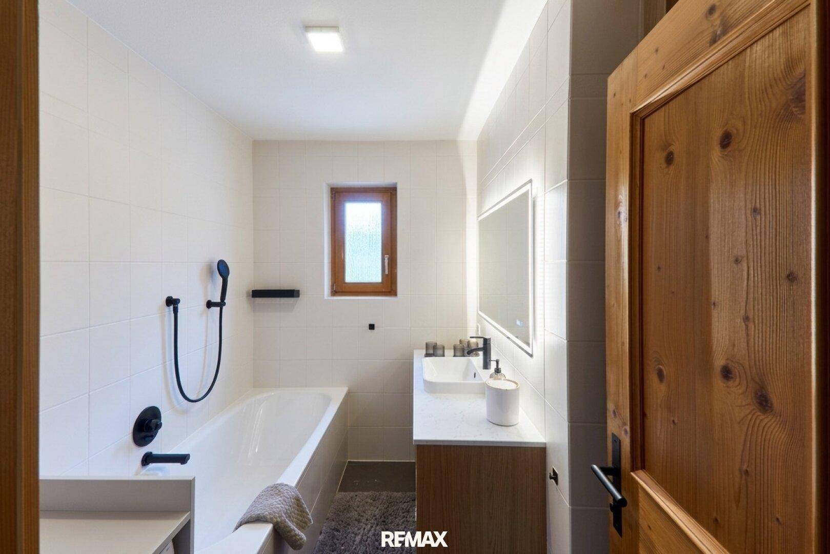 Modernes Badezimmer mit Badewanne, Einzelwaschbecken und weißen Fliesen.
