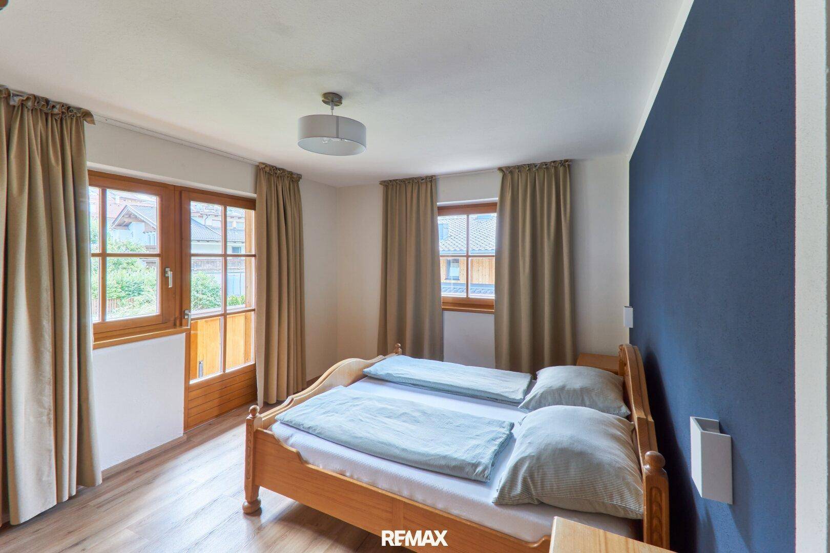 Schlafzimmer mit Holzbett, Laminatboden und Zugang zu einem kleinen Balkon.