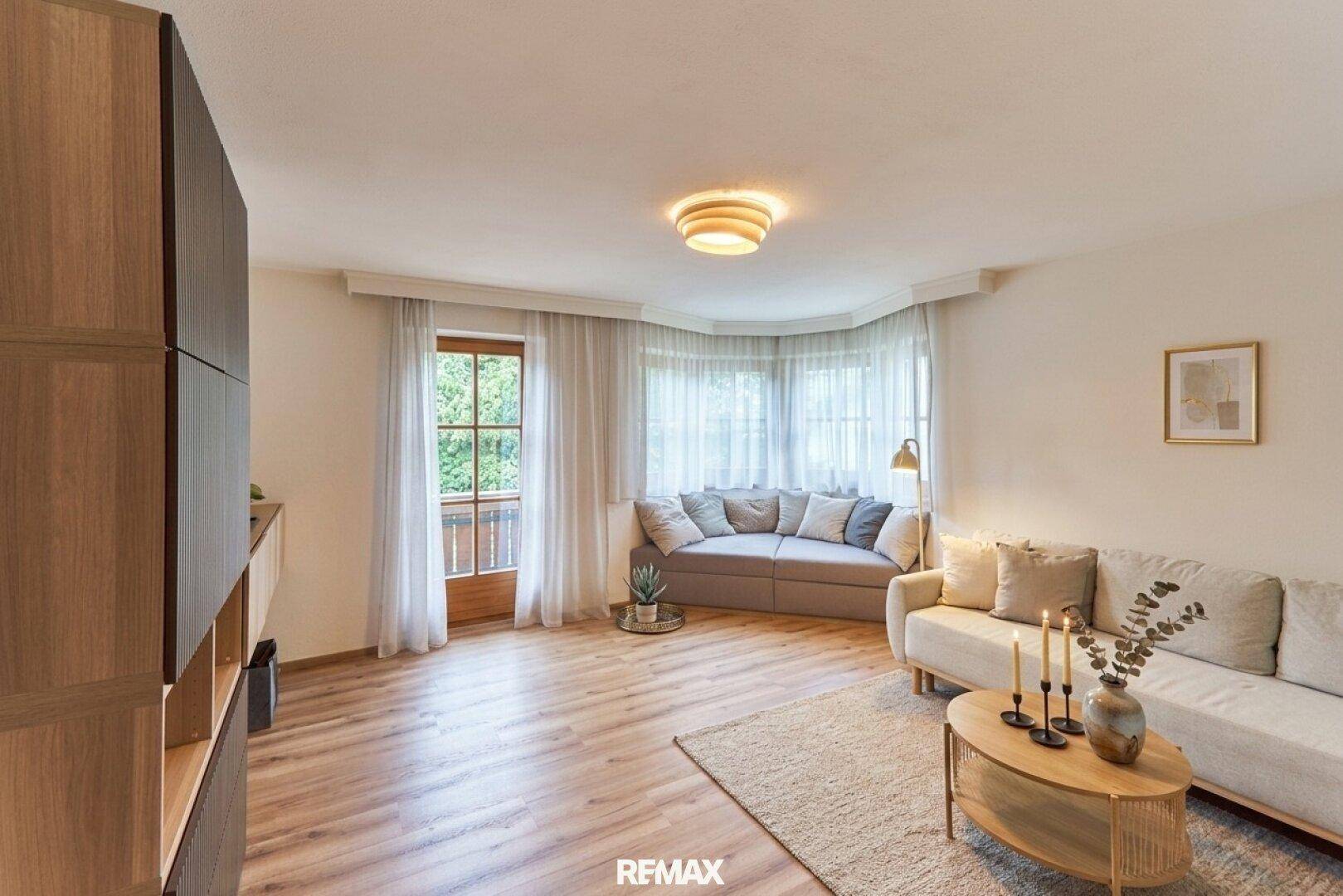 Helles Wohnzimmer mit modernem Laminatboden, beigen Sofas und Zugang zum Balkon.