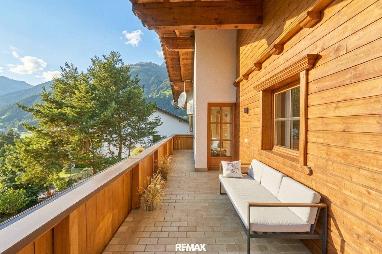 Langer Holzbalkon mit Sitzbank und weitem Blick auf die Berge und das Tal.