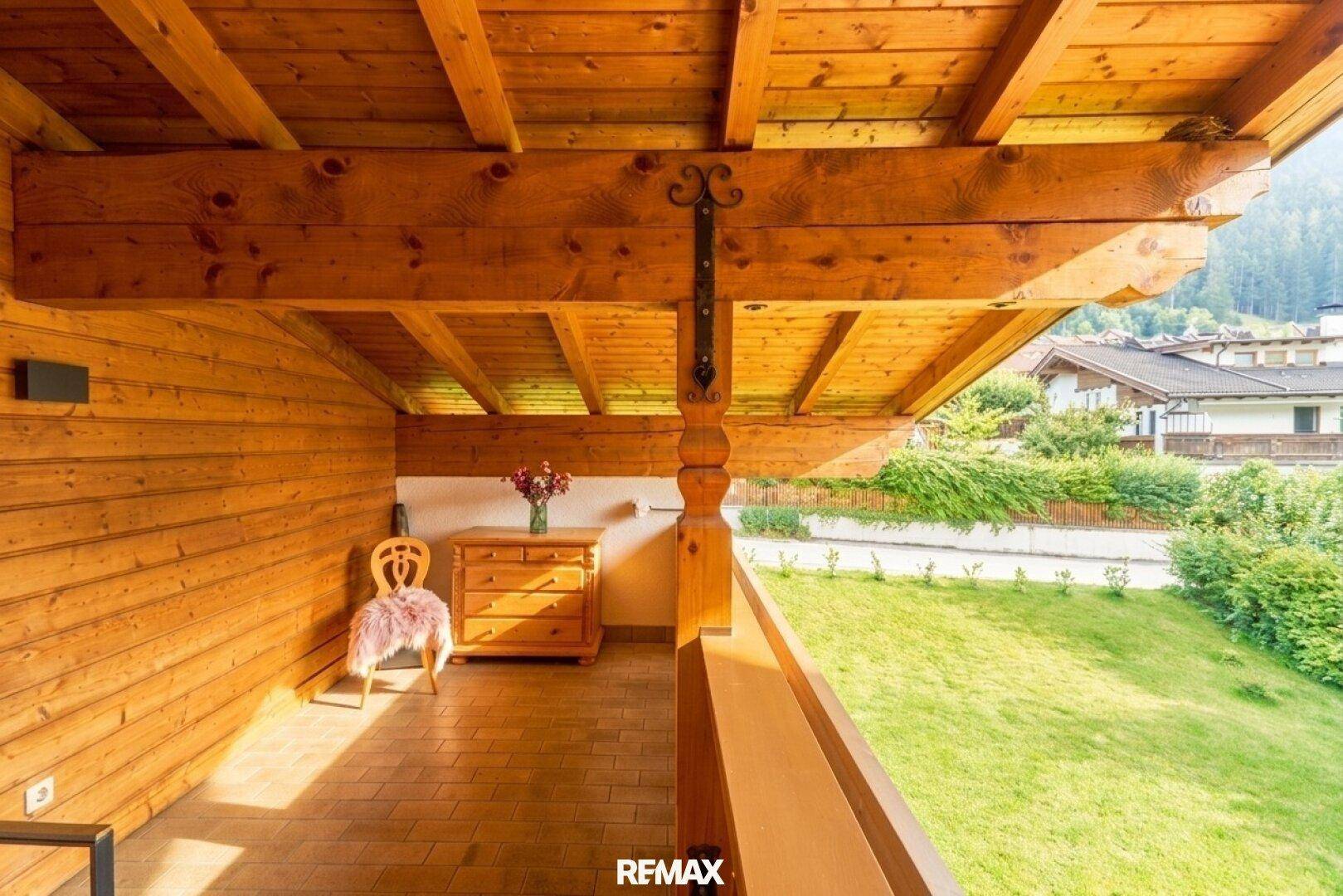 Überdachter Holzbalkon mit rustikalen Möbeln und Blick auf die grüne Umgebung.