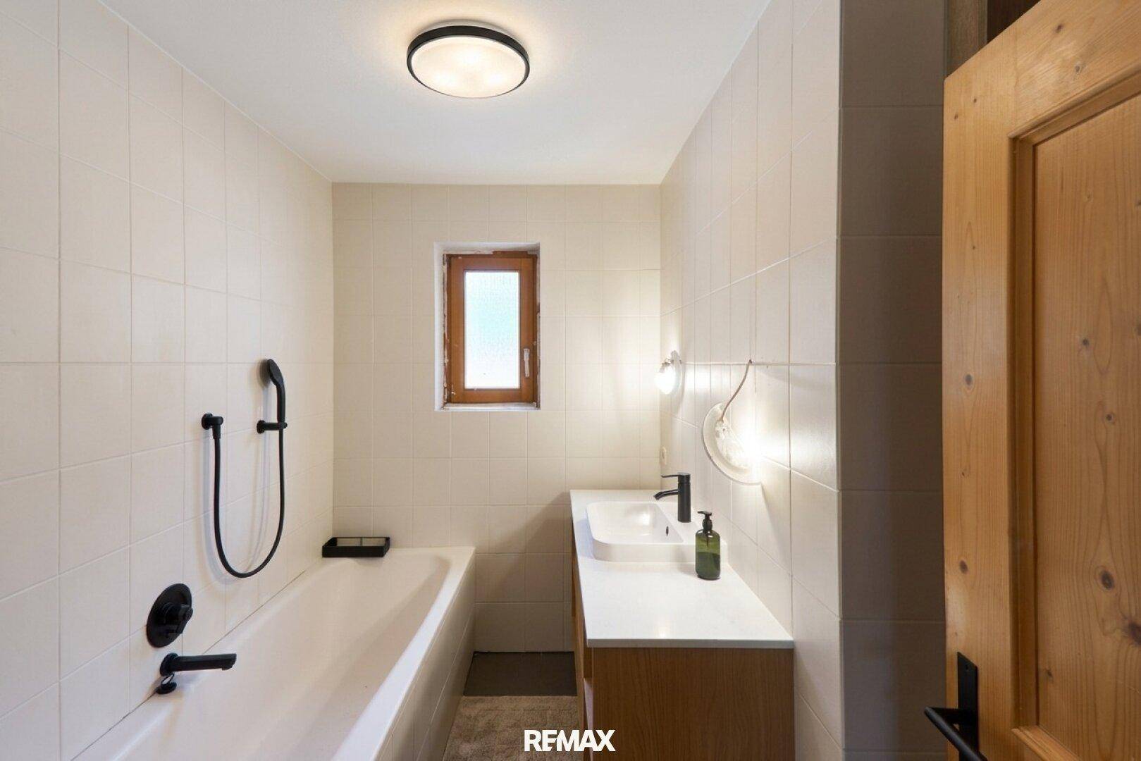 Modernes Badezimmer mit Badewanne, Einzelwaschbecken und weißen Fliesen.