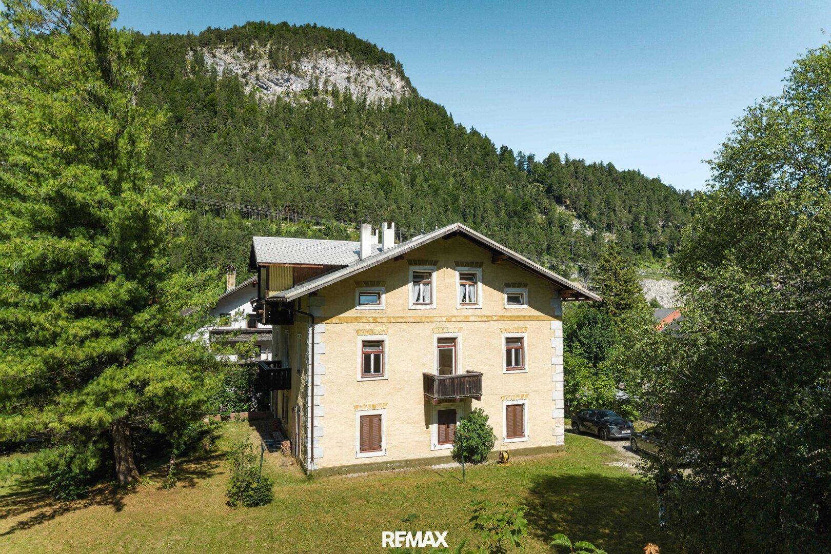 Traditionelles Haus mit gelber Fassade, Holzbalkonen und Blick auf die umliegenden Berge.