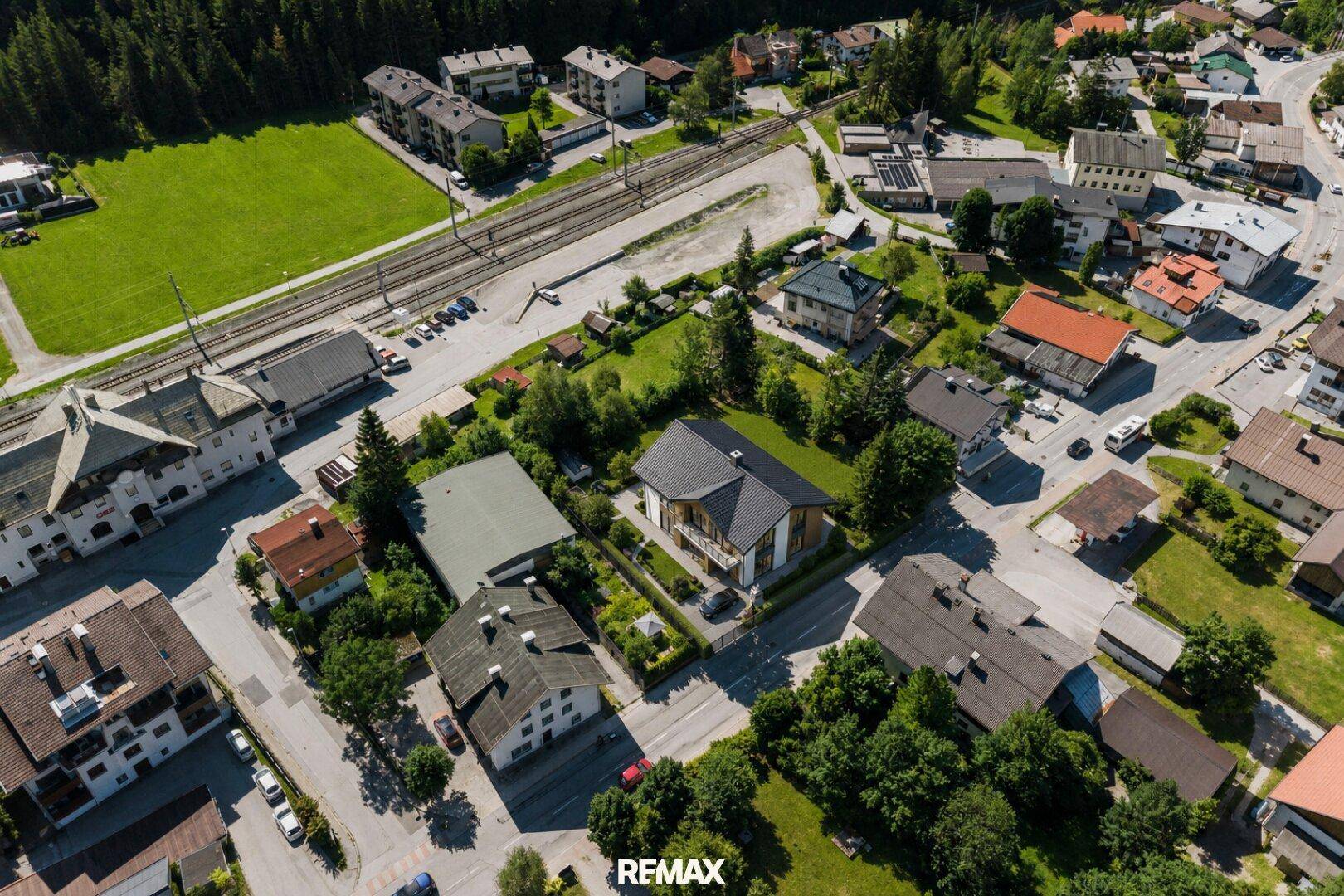 Luftaufnahme einer ländlichen Siedlung mit Wohnhäusern, Grünflächen und Bahngleisen.