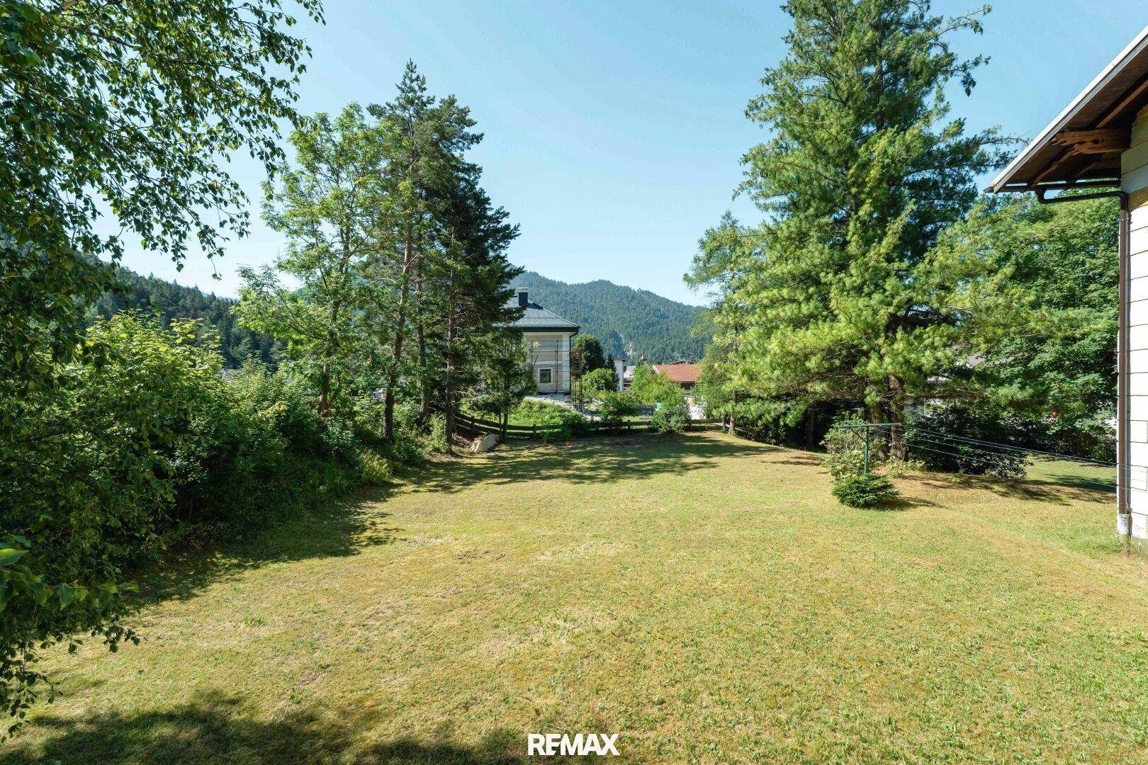 Weitläufige Rasenfläche mit hohen Bäumen und Blick auf die umliegende Berglandschaft.