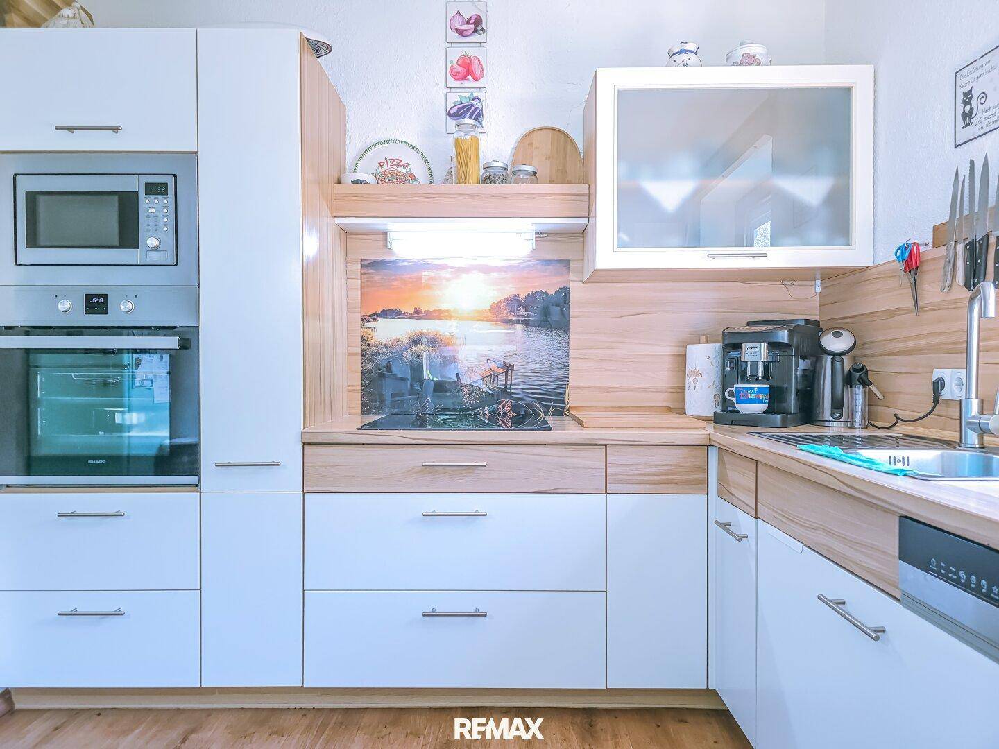 Moderne Einbauküche mit weißen Fronten, Holzakzenten und integrierter Kaffeemaschine.