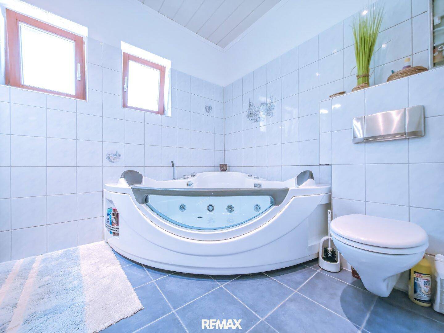 Geräumiges Badezimmer mit Whirlpool-Badewanne, blauen Fliesen und zwei Fenstern.