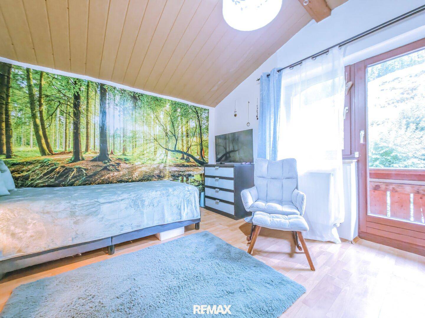 Gemütliches Schlafzimmer mit Holzbalkendecke, Waldtapete und Zugang zum Balkon.