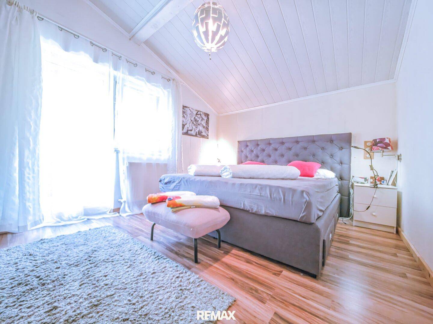 Helles Schlafzimmer mit großem Bett, Holzbalkendecke und viel Tageslicht.