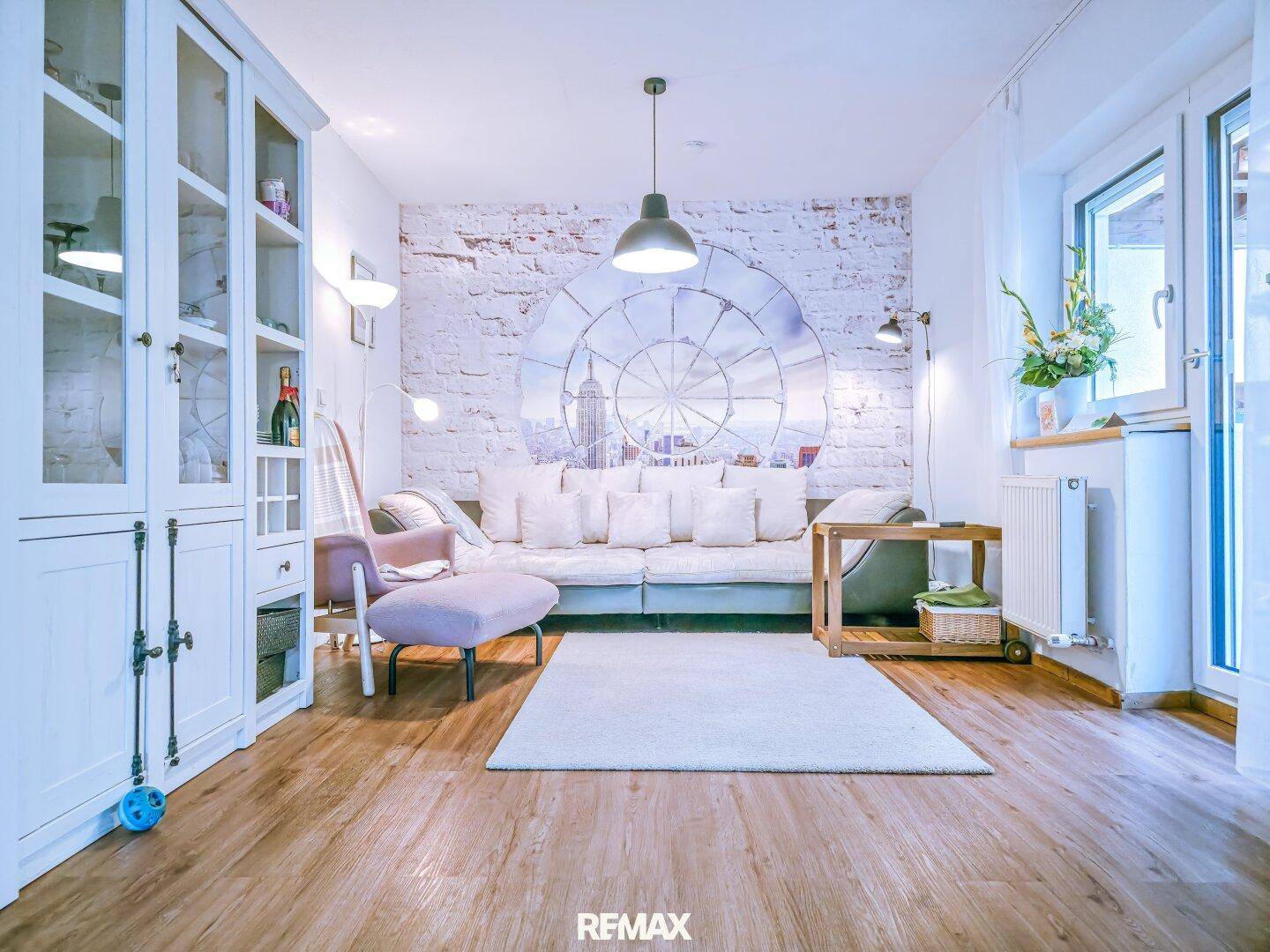 Modernes Wohnzimmer mit bequemer Couch, Holzboden und dekorativer Wandgestaltung.