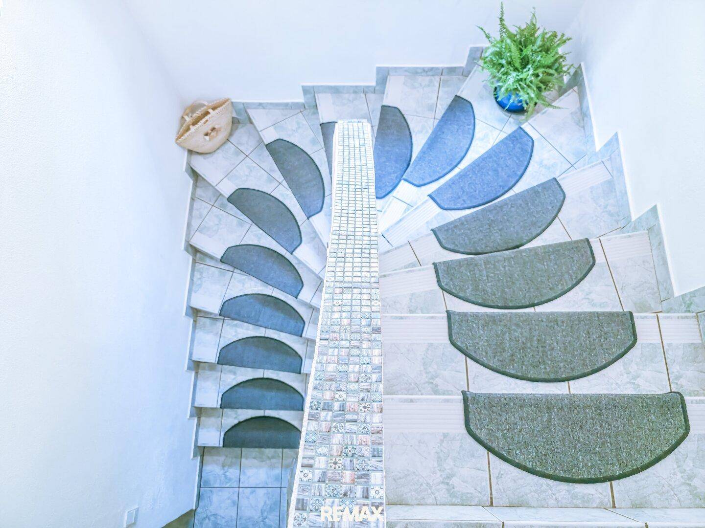 Wendeltreppe mit Fliesenstufen und dekorativer Mosaikverkleidung, die die Etagen verbindet.