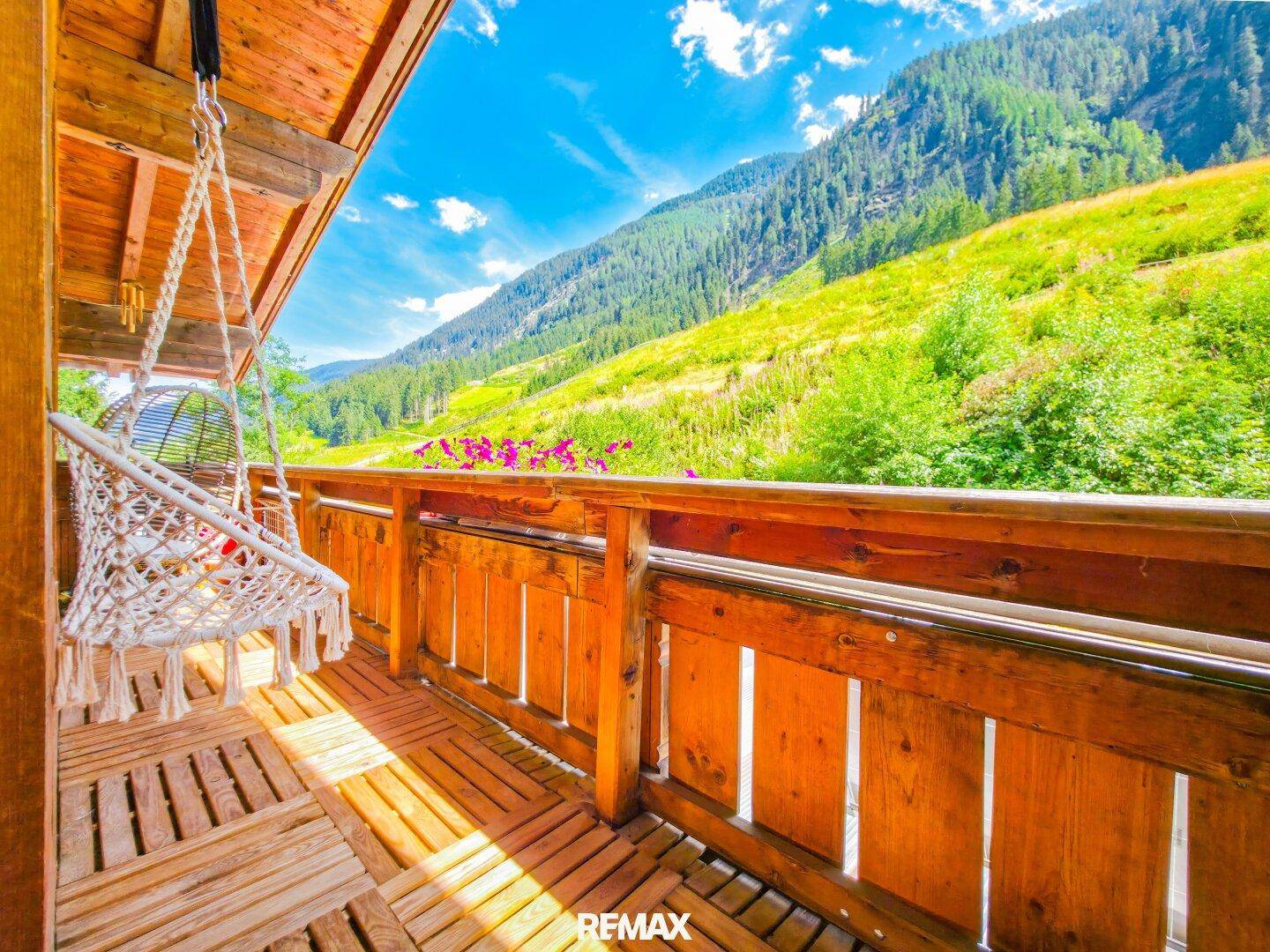 Gemütlicher Holzbalkon mit Hängesessel und atemberaubendem Blick auf die umliegenden Berge.