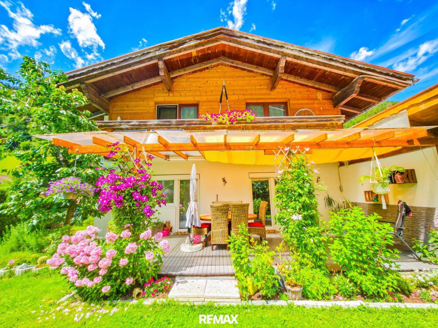 Charmantes Haus mit Holzfassade, einer blühenden Terrasse und einem gepflegten Gartenbereich.
