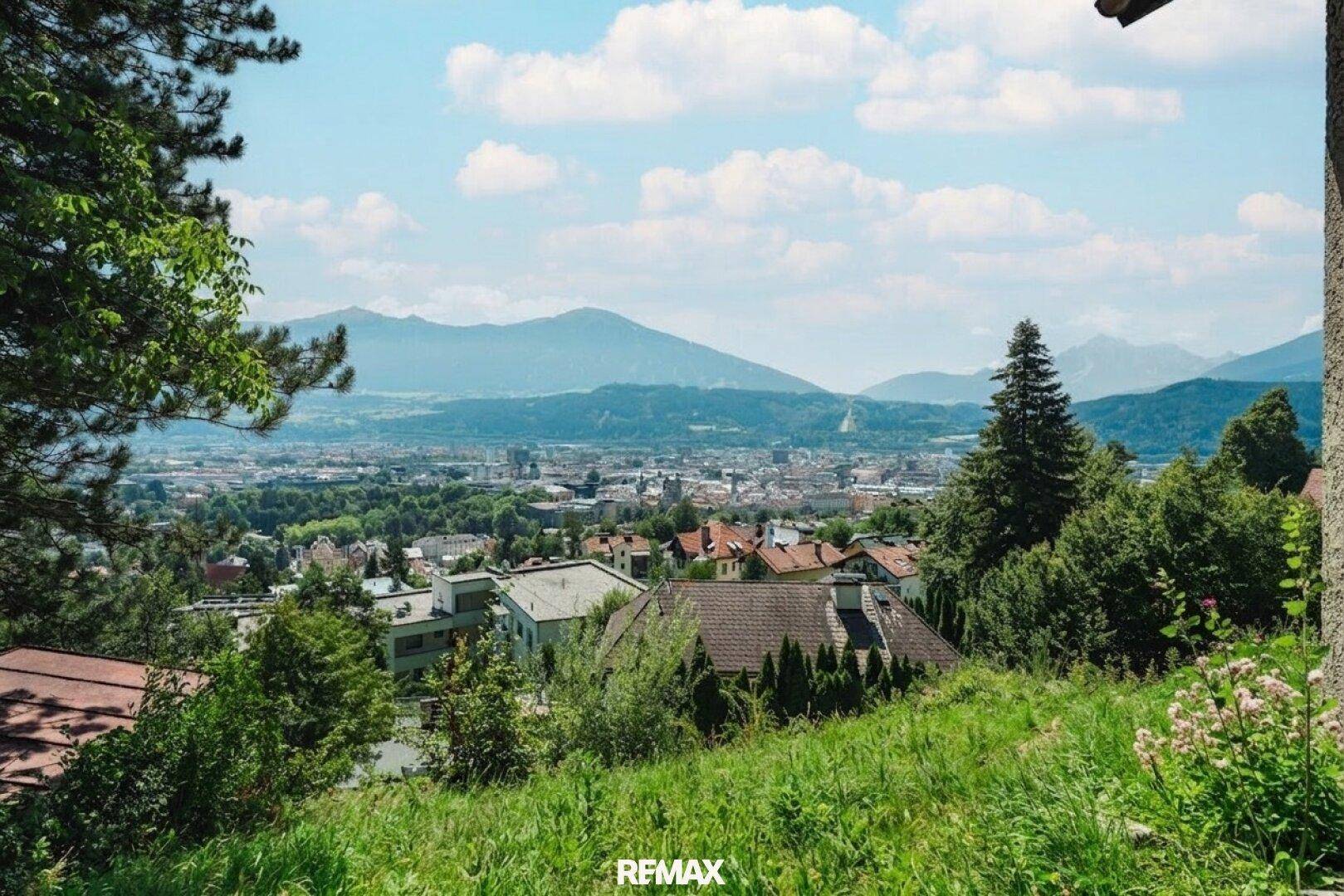 Malerischer Panoramablick über die Stadt im Tal, umgeben von majestätischen Bergen und grüner Natur.