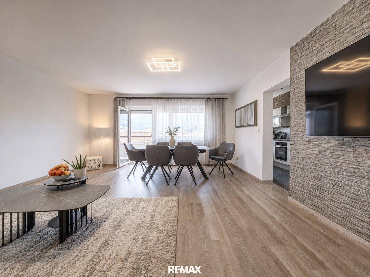 Heller Wohn-Essbereich mit Zugang zum Balkon, modernem Esstisch und Blick auf die umliegende Landschaft.