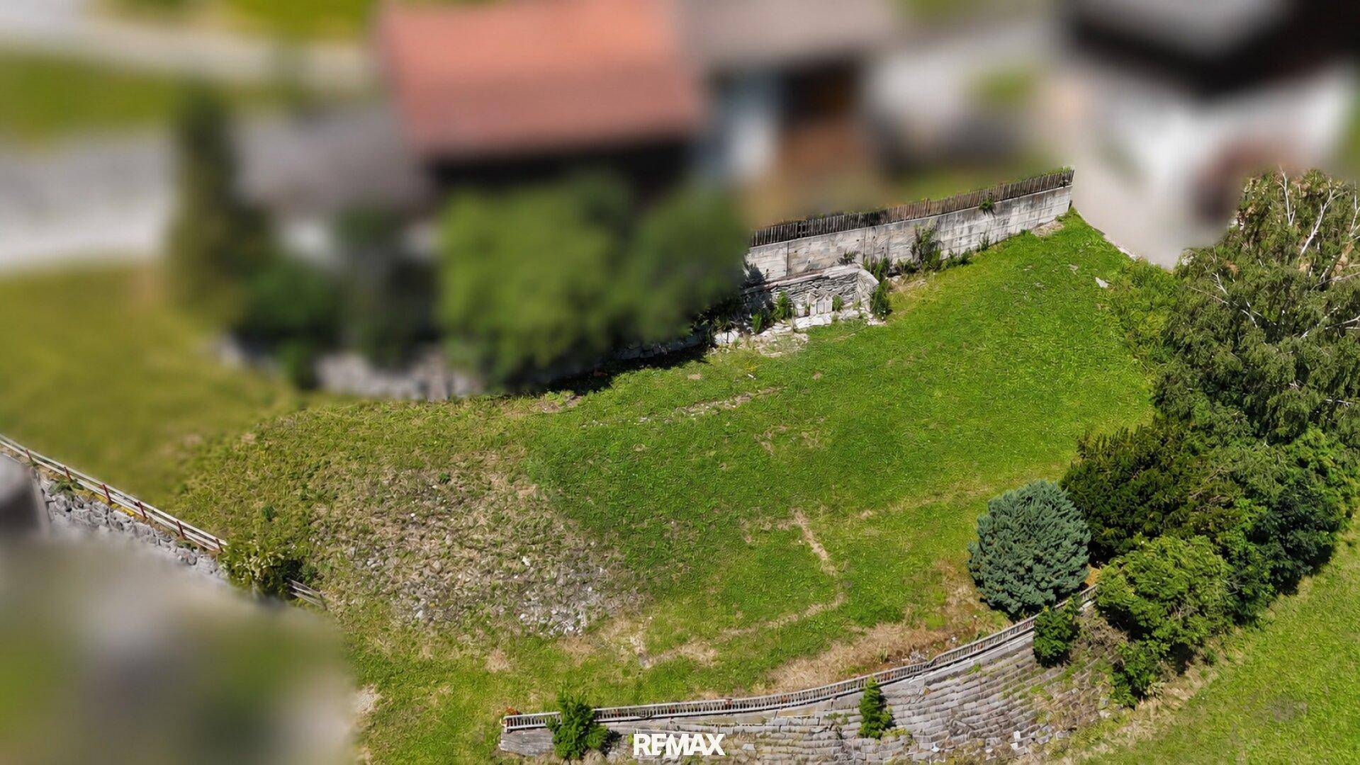 Weitläufiges grünes Grundstück mit sanften Hängen, Bäumen und historischen Stützmauern.