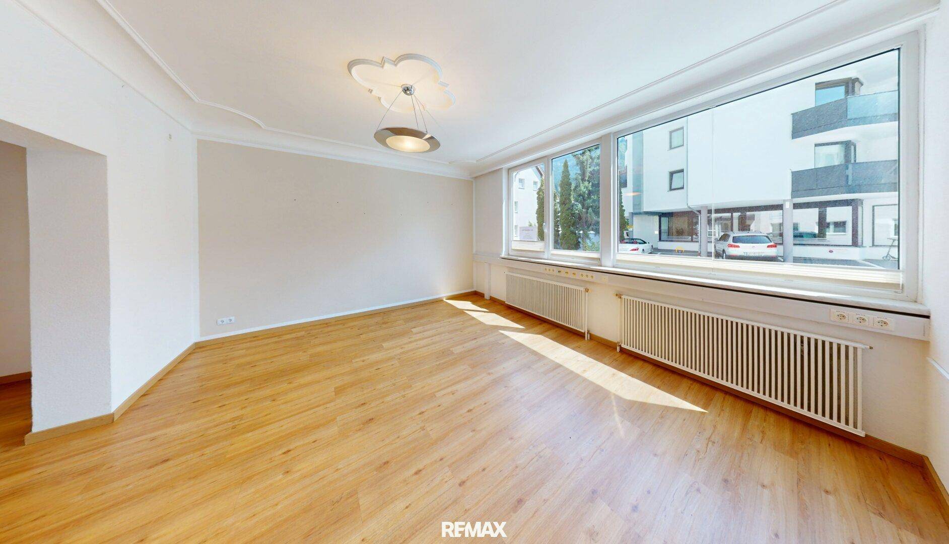 Heller, leerer Büroraum mit großen Fenstern, Laminatboden und viel Tageslicht.
