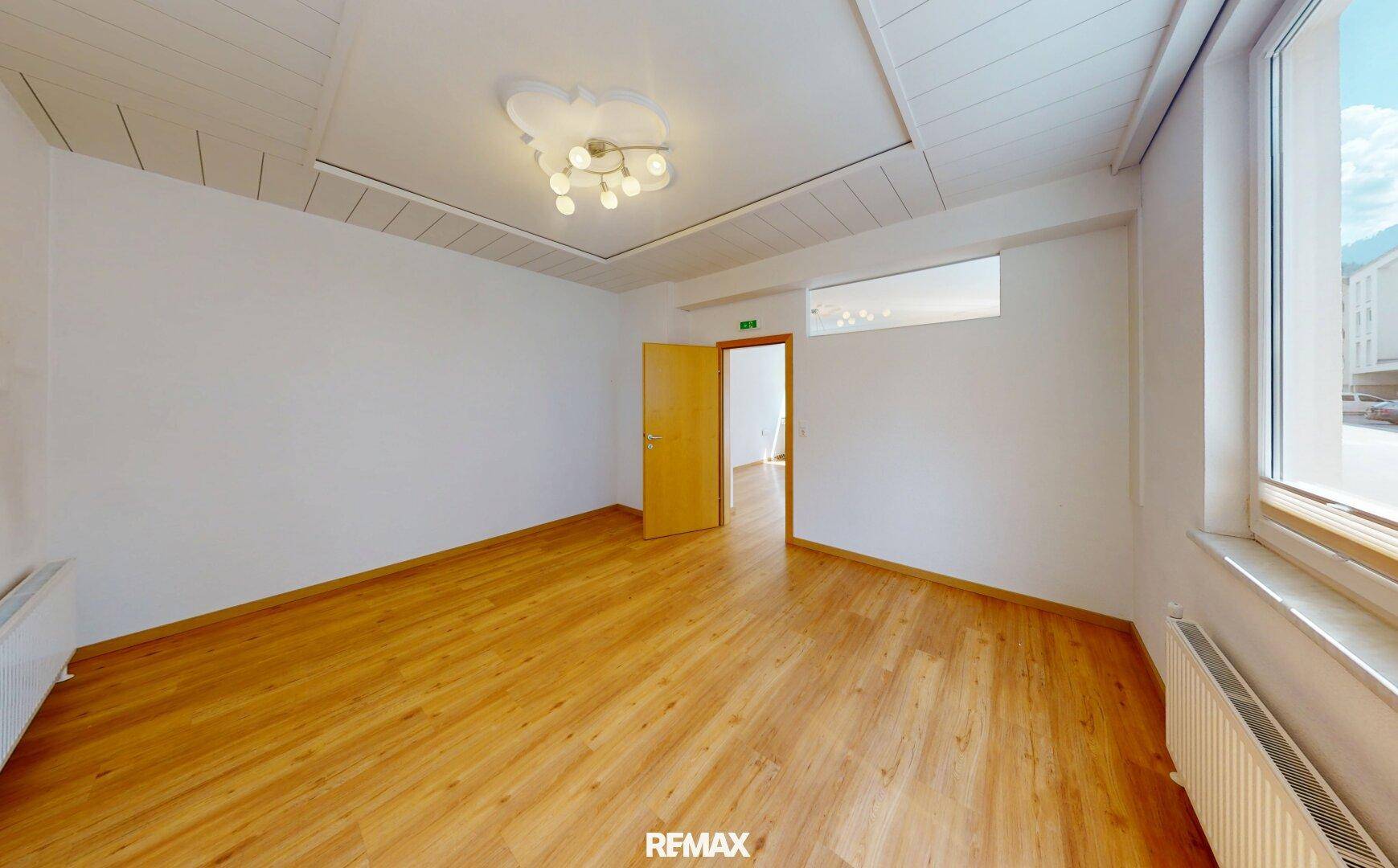 Leerer Raum mit Laminatboden, weißen Wänden und einer Holzlattendecke, ideal für ein Büro.
