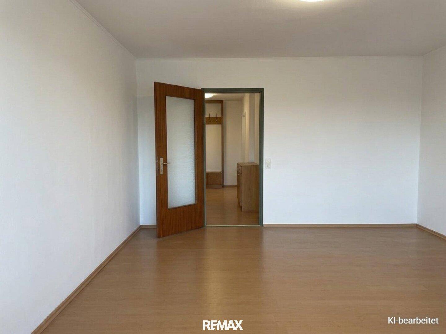 Leerer Raum mit Laminatboden und einer Holztür, die zu einem weiteren Bereich führt.