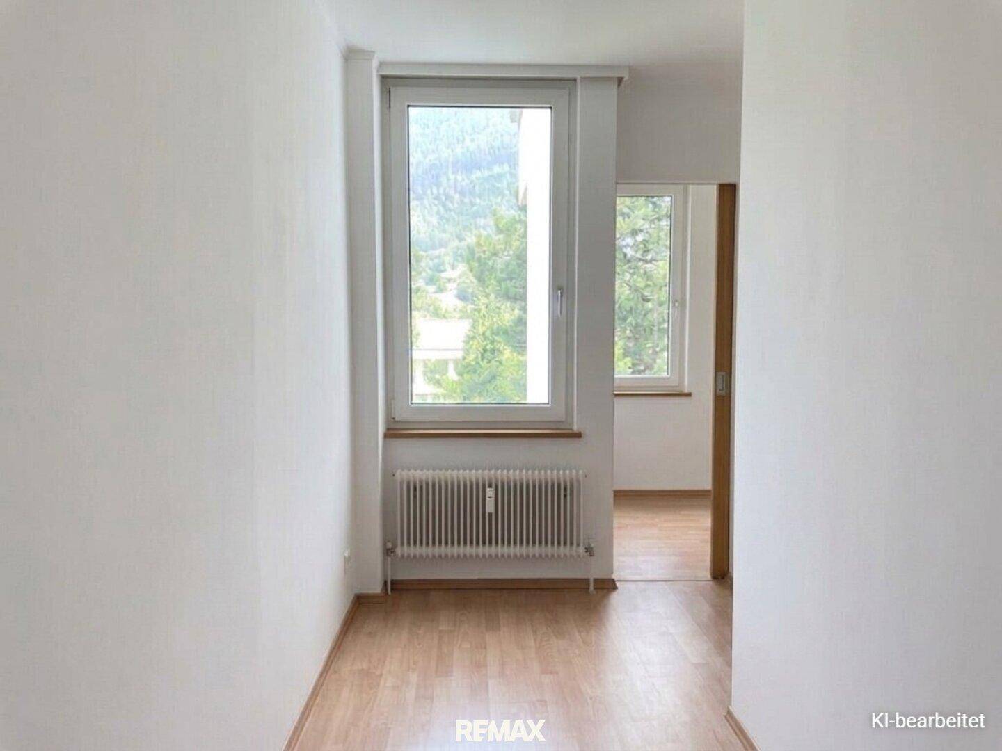 Heller, leerer Raum mit Laminatboden und einem Fenster mit Blick ins Grüne.