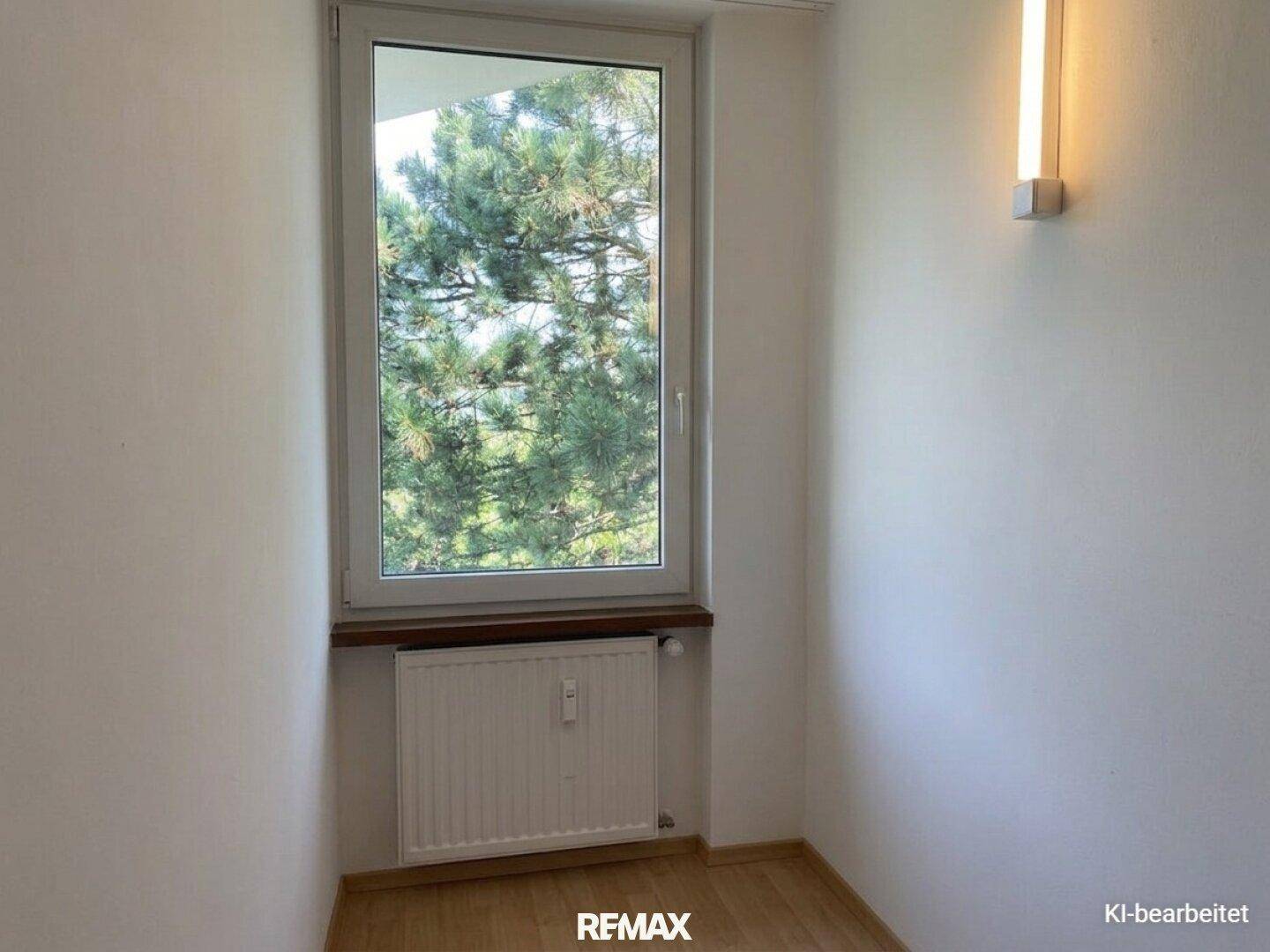 Heller Raum mit Laminatboden und einem Fenster, das einen angenehmen Blick ins Grüne bietet.