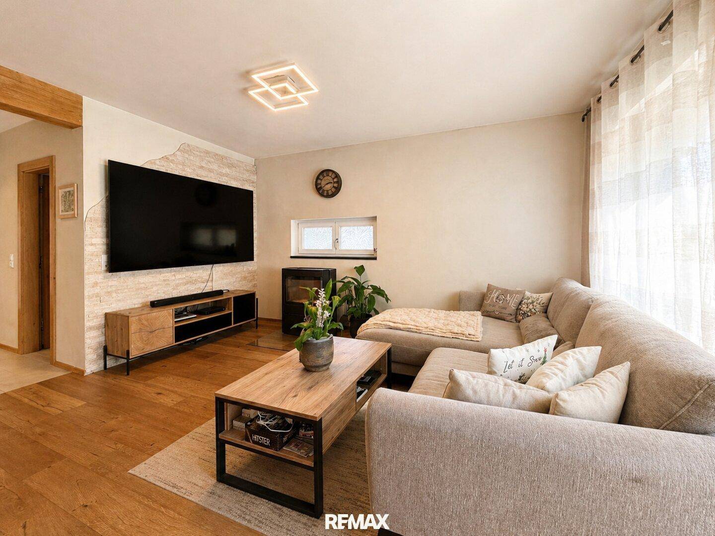 Gemütliches Wohnzimmer mit großem Sofa, Holzboden und einem modernen Kaminofen.