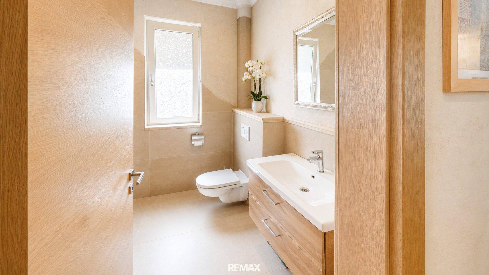 Helles Gäste-WC mit Waschbecken, Toilette und Fenster, modern gefliest.