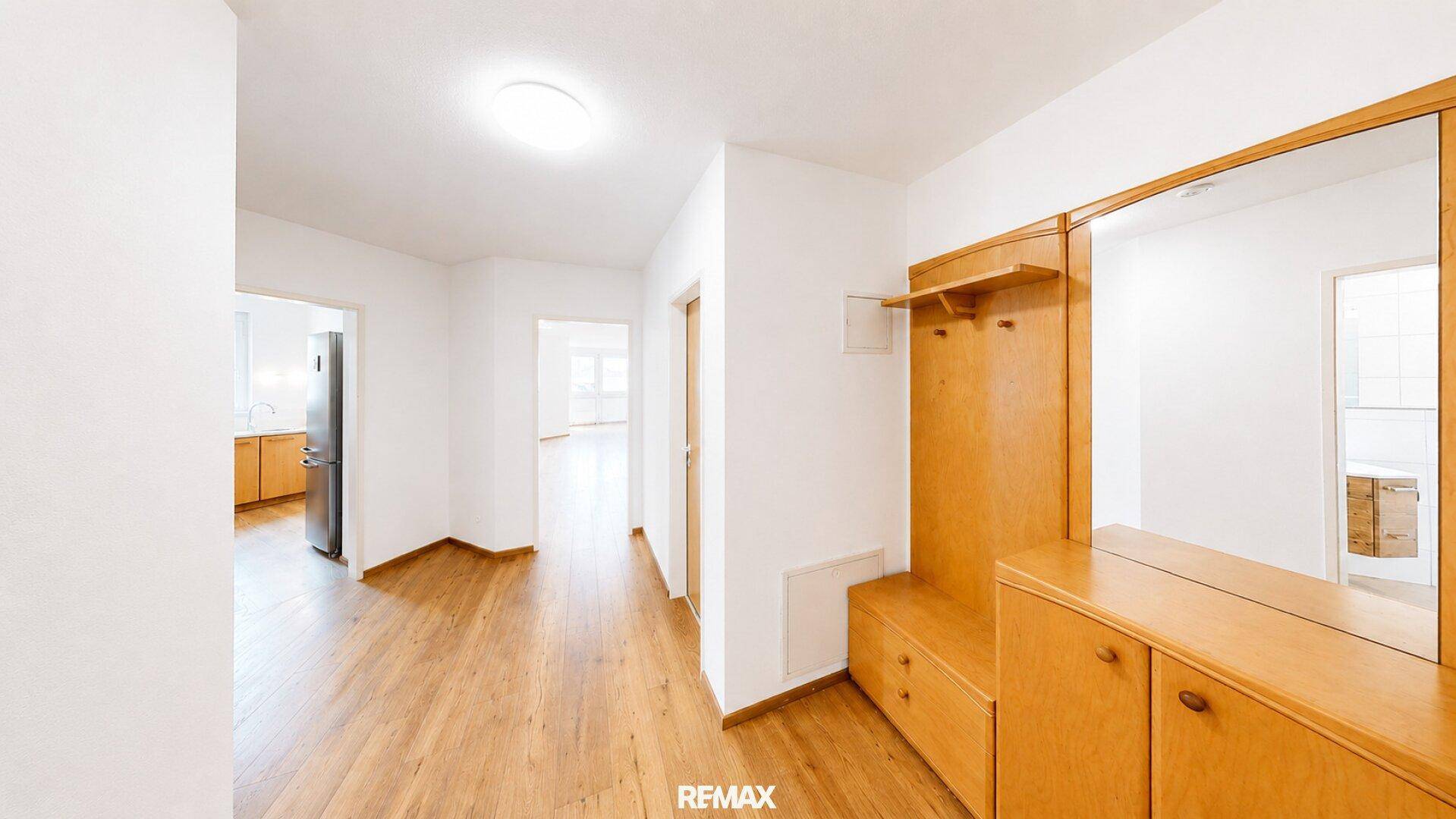 Heller Flur mit Holzparkett und einer Garderobe mit Spiegel, die zu weiteren Räumen führt.