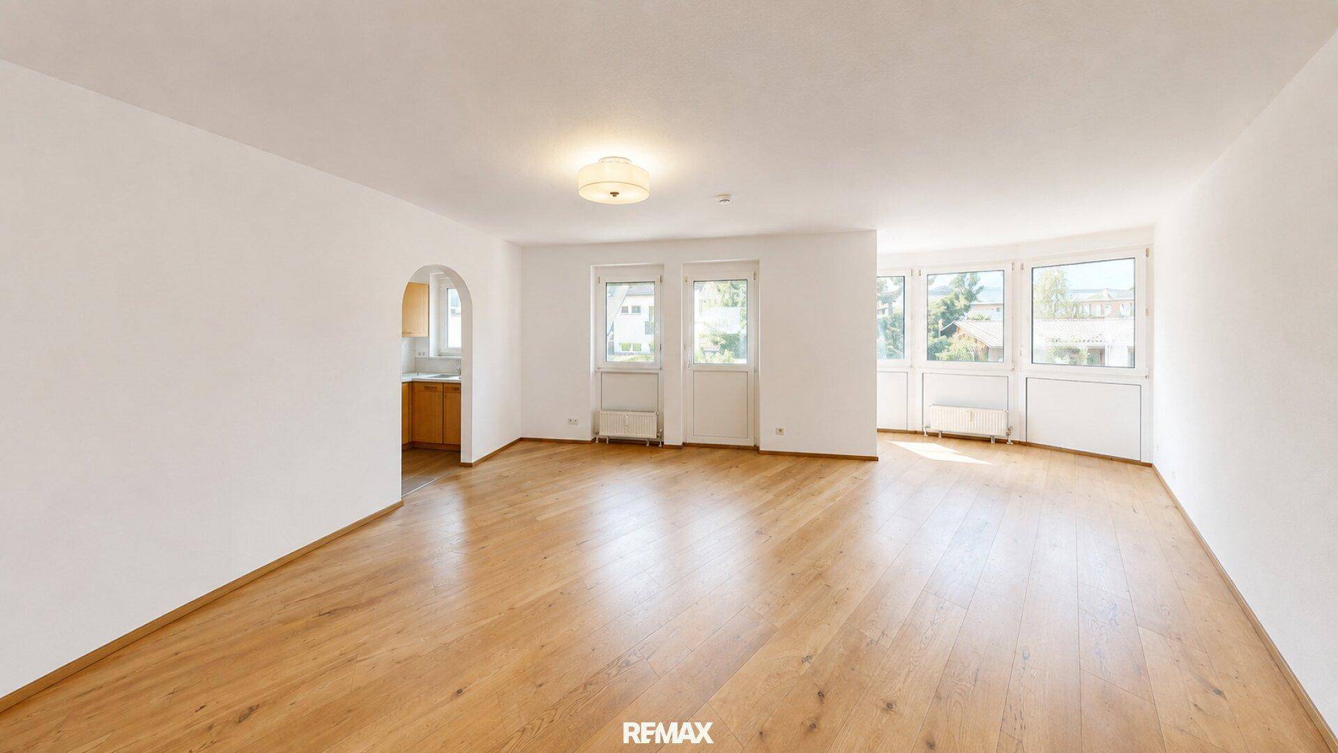 Geräumiges, leeres Wohnzimmer mit Parkettboden und vielen Fenstern, die den Raum hell erscheinen lassen.