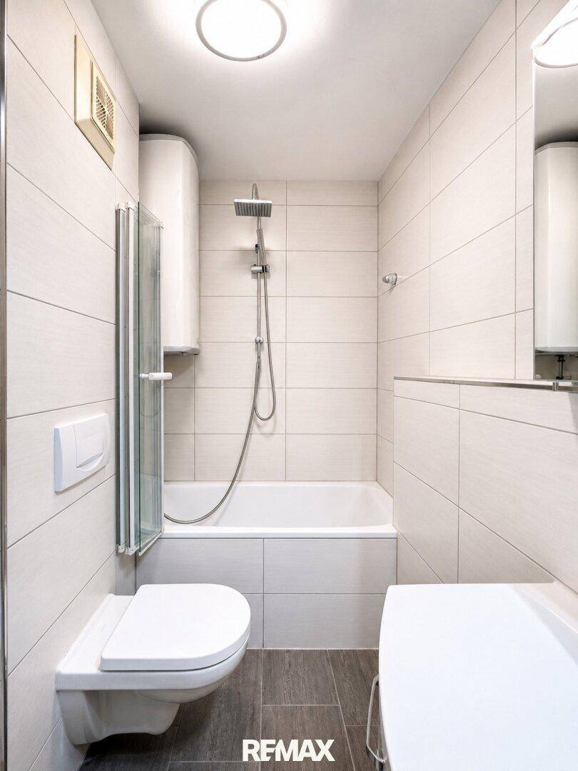 Kompaktes Badezimmer mit Badewanne, integrierter Dusche und wandhängendem WC, komplett gefliest.